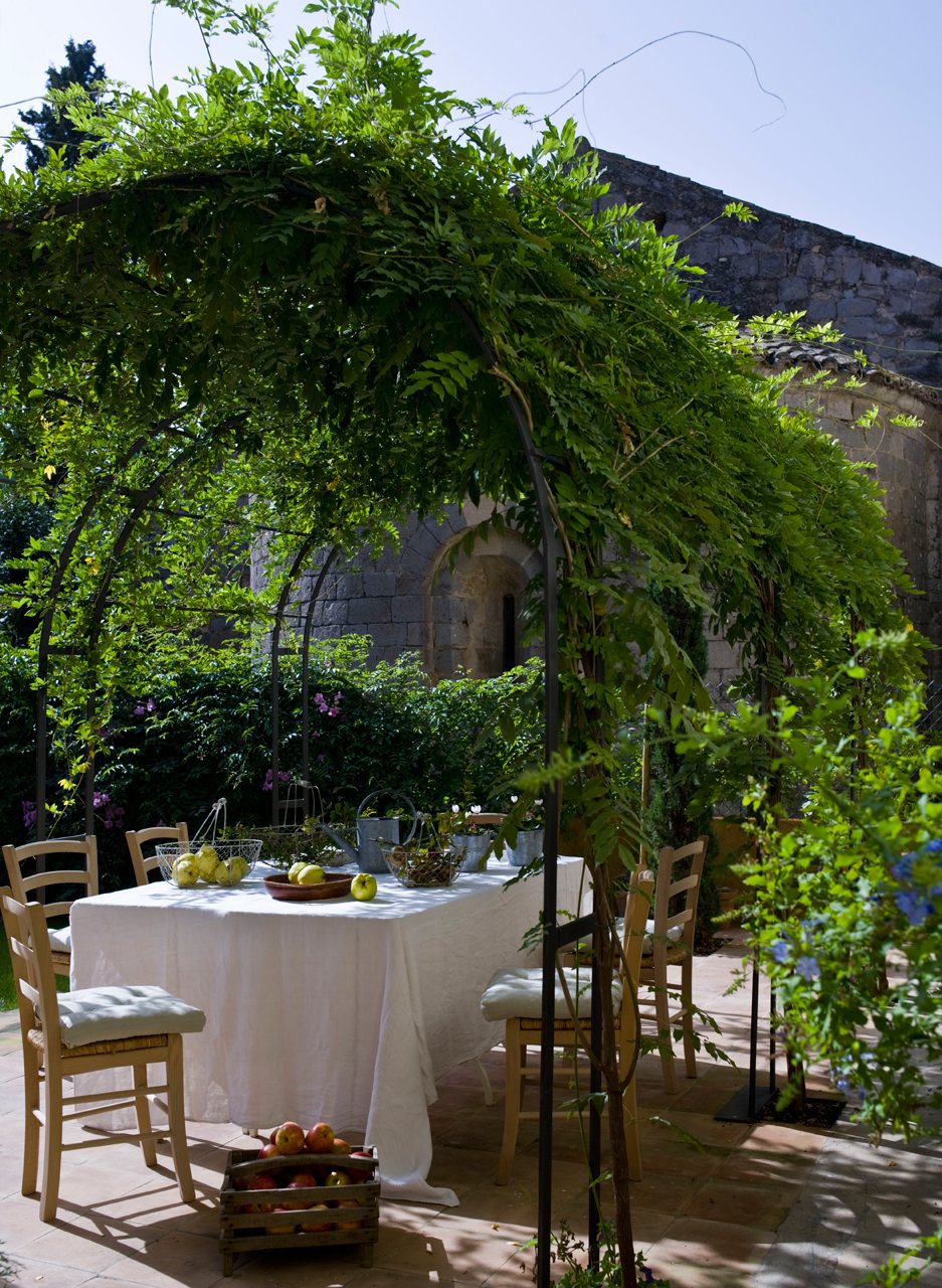 Comedor exterior con techo natural y rodeado de plantas trepadoras. 