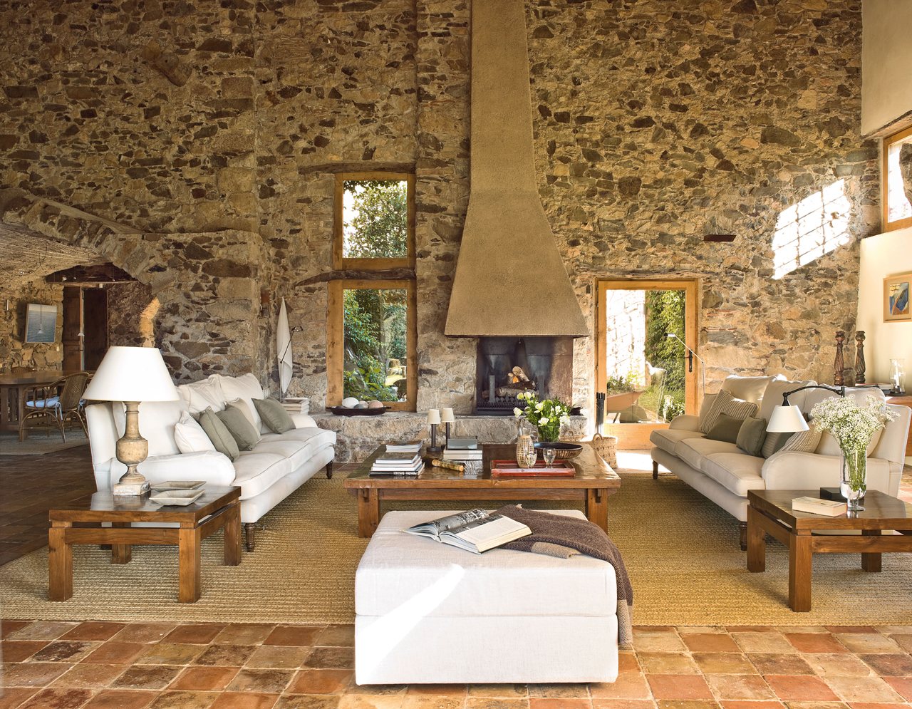 Salón de estilo rústico con paredes de piedra, chimenea y sofás blancos.