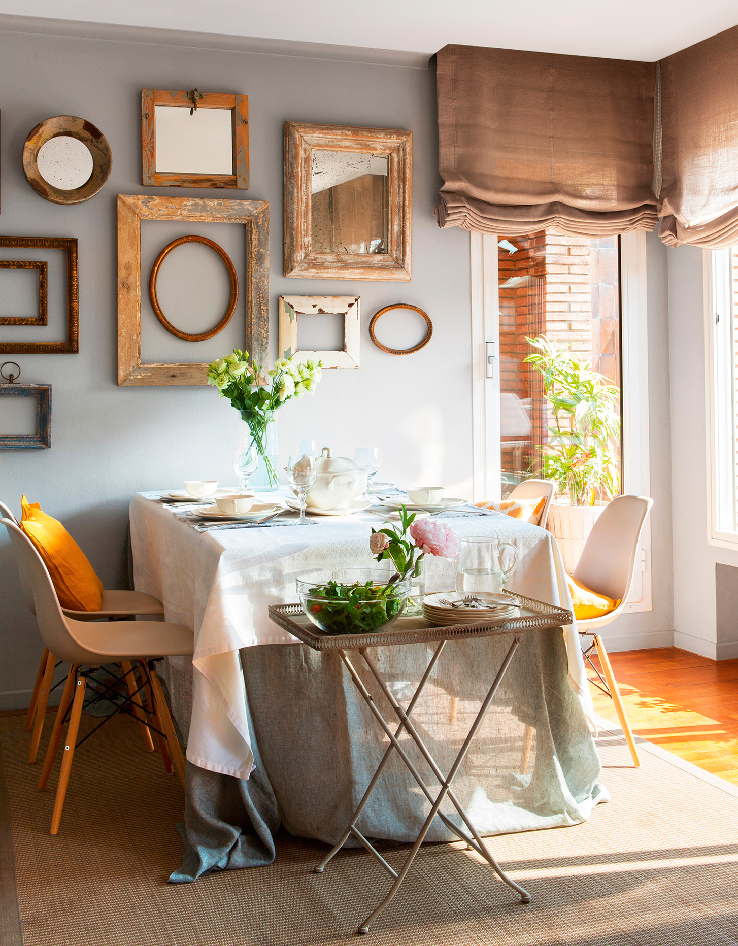 Comedor pequeño con mesa pegada a la pared, decorada con espejos y marcos de cuadros. 