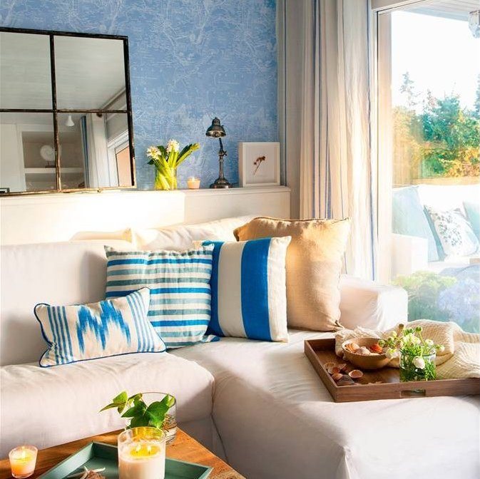 Salón con sofá blanco, pared azul, cojines a rayas e ikat, bandeja de madera y espejo 