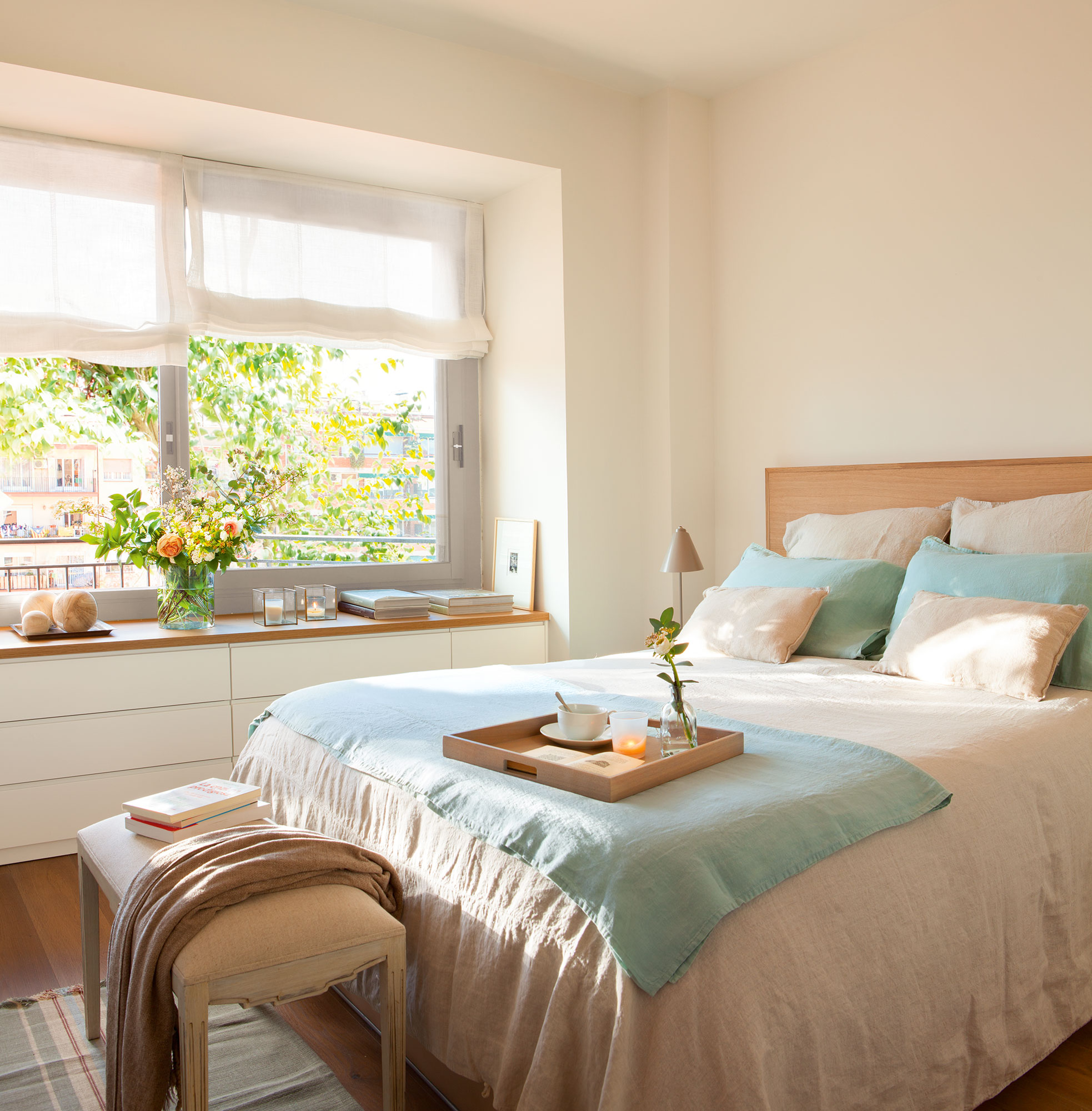 Dormitorio con cabecero de madera y mueble a medida bajo la ventana. 