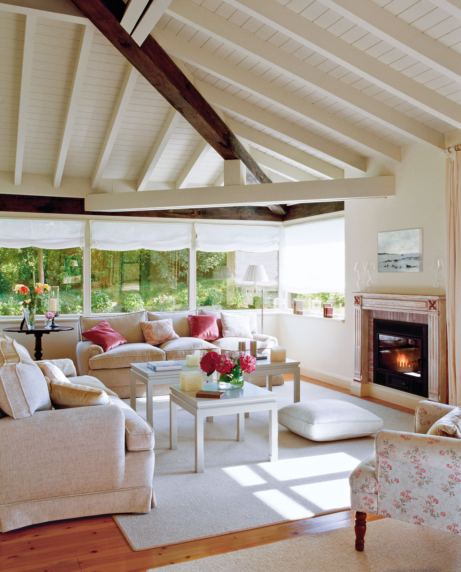 Salón con techos abuhardillados de madera, sofás blancos y chimenea. 
