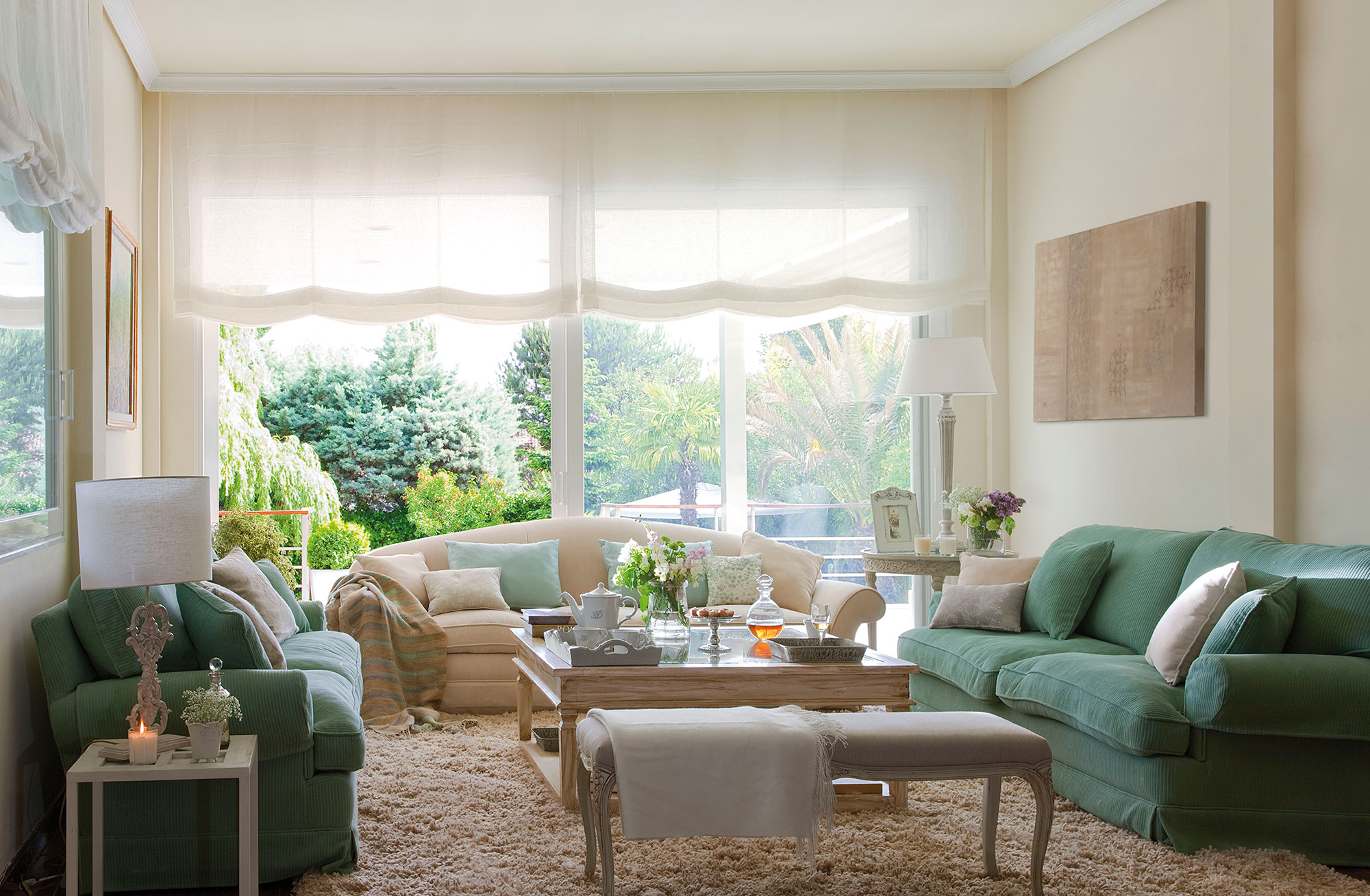 Salón con vistas al jardín y con un sofá beige y dos verdes.