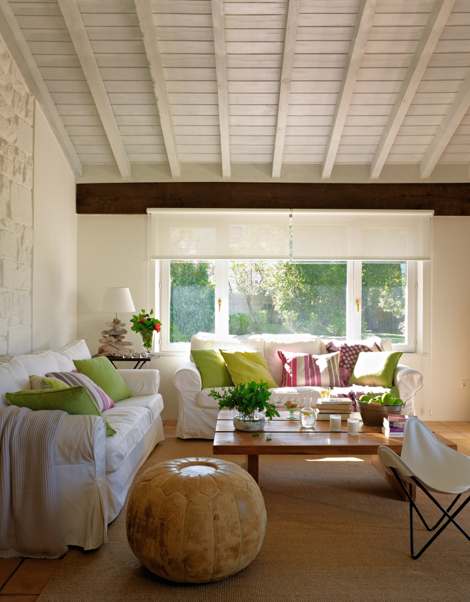 Salón con vigas de madera pintadas en blanco y ventanal al porche