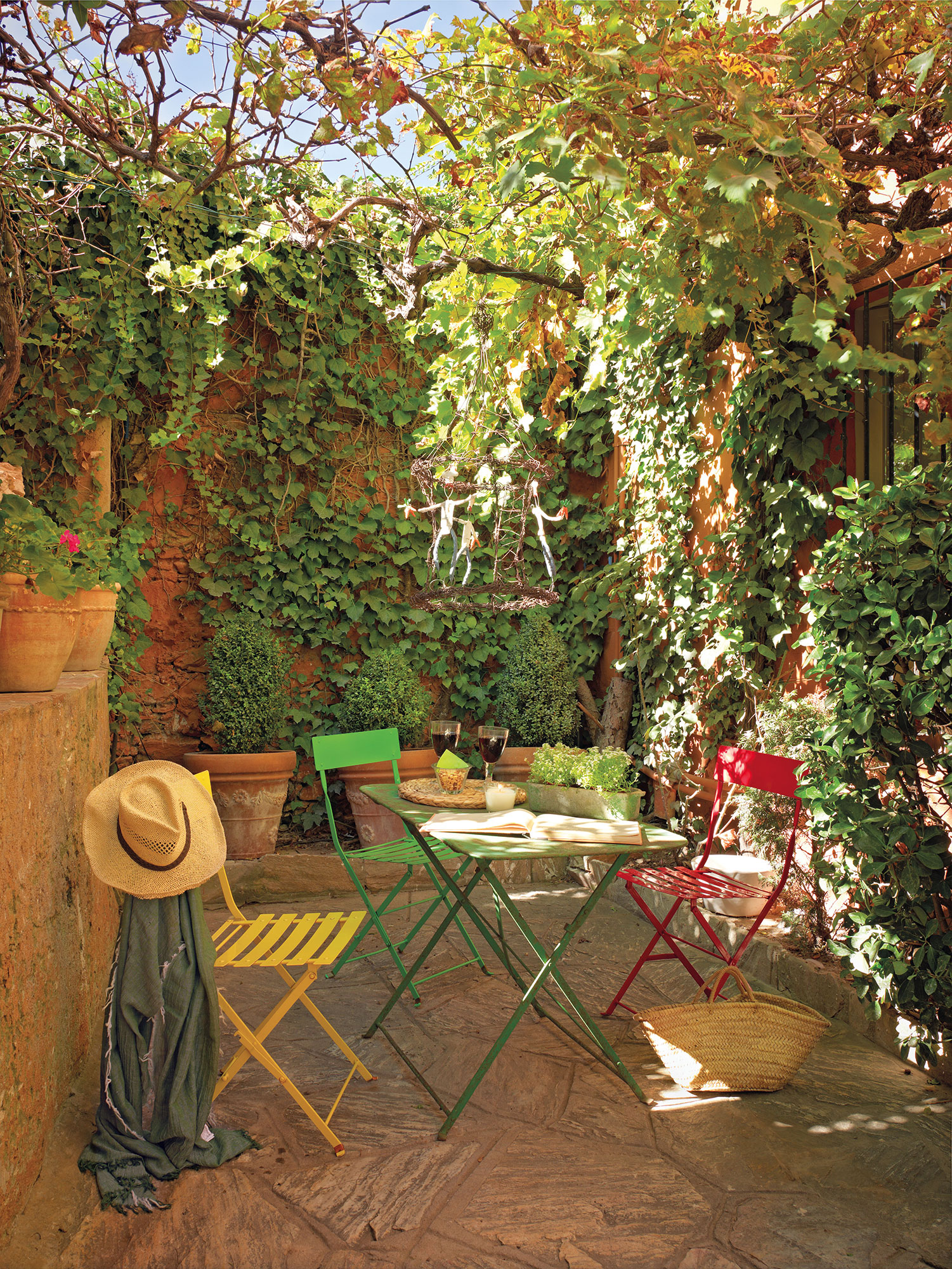 Un patio con mesas de colores y muchas enredaderas.