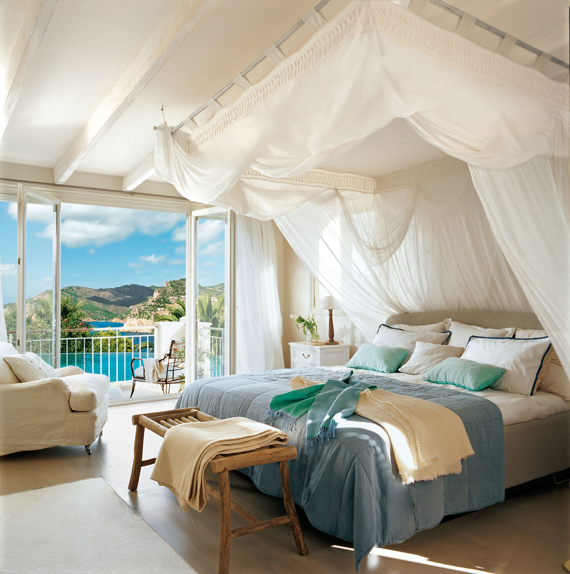 Dormitorio de verano con dosel y cortinas y ropa de cama azul y blanca. 