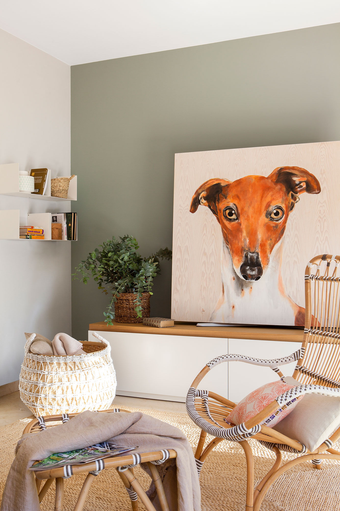 Salón decorado con alfombra de fibras, gran cuadro de un perro, pared verde y cesto con mantas.