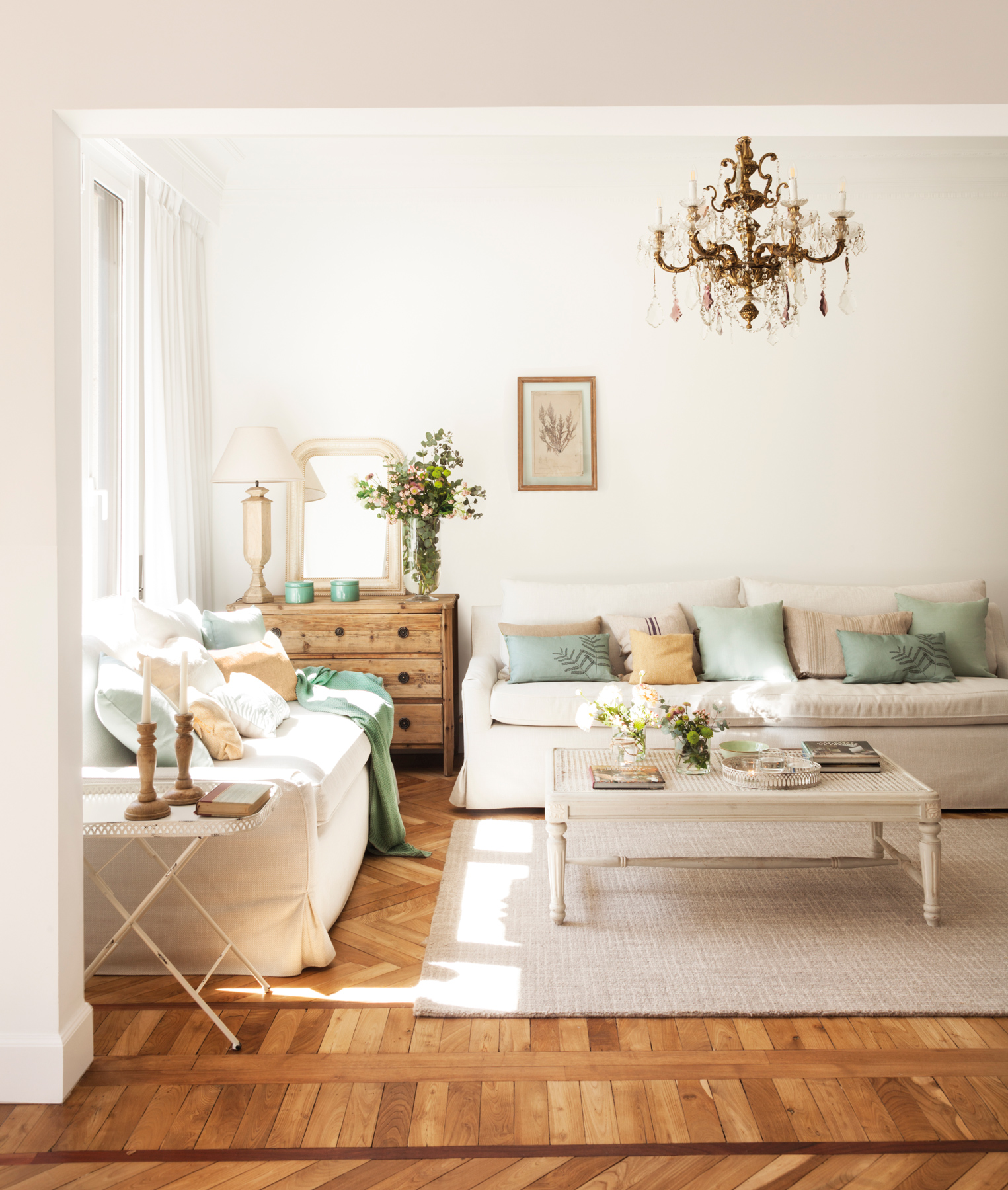 Salón clásico con suelos de madera, sofás blancos y l��mpara de araña. 