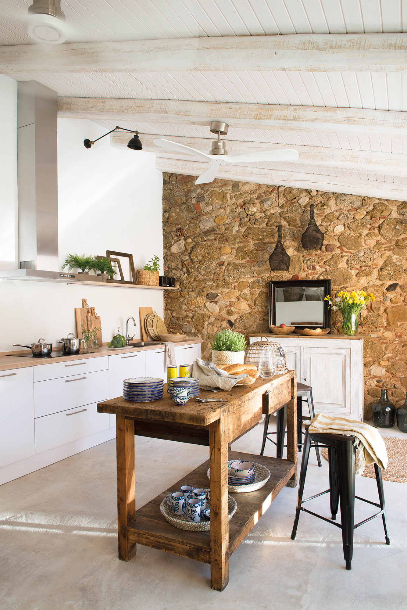 Cocina blanca con muebles modernos, paredes de piedra e isla con aparador de madera recuperado.
