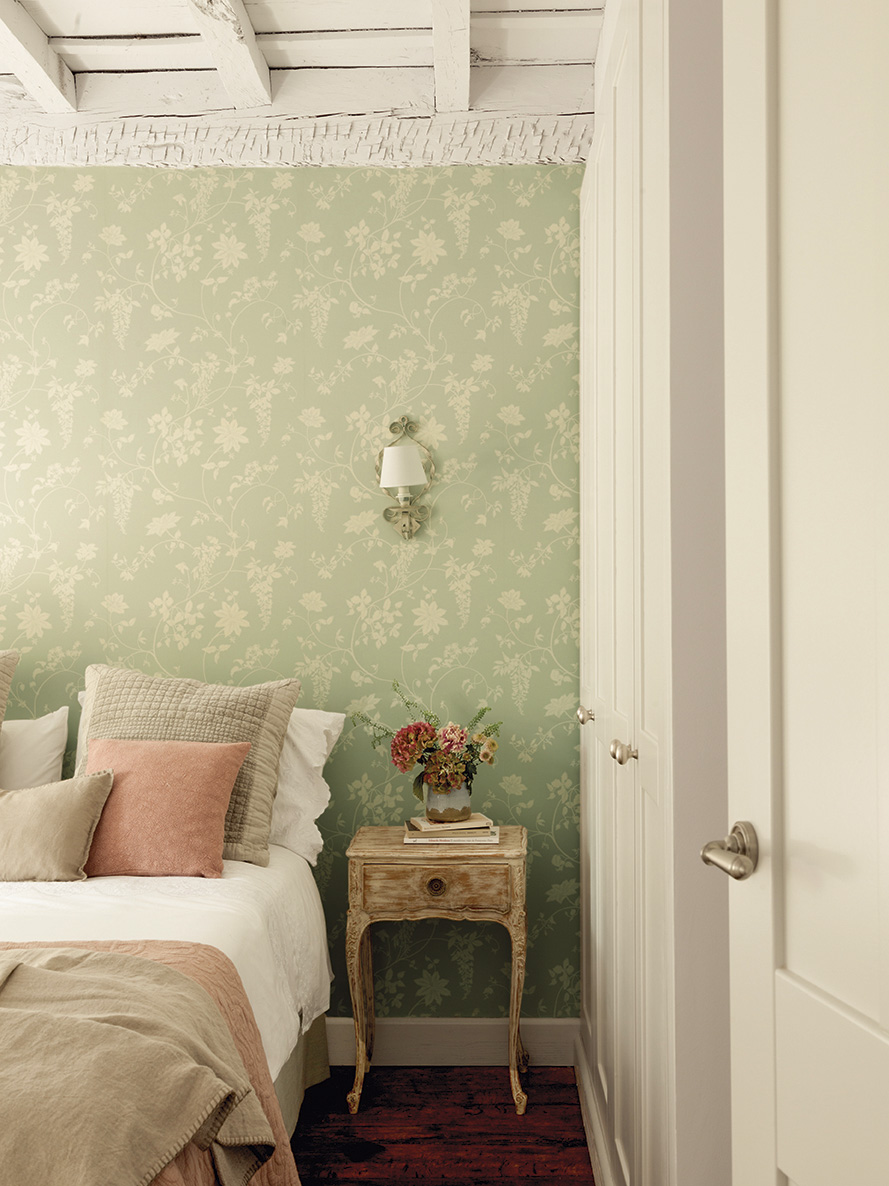 Dormitorio con armarios blancos y papel pintado floral verde en la pared del cabecero. 