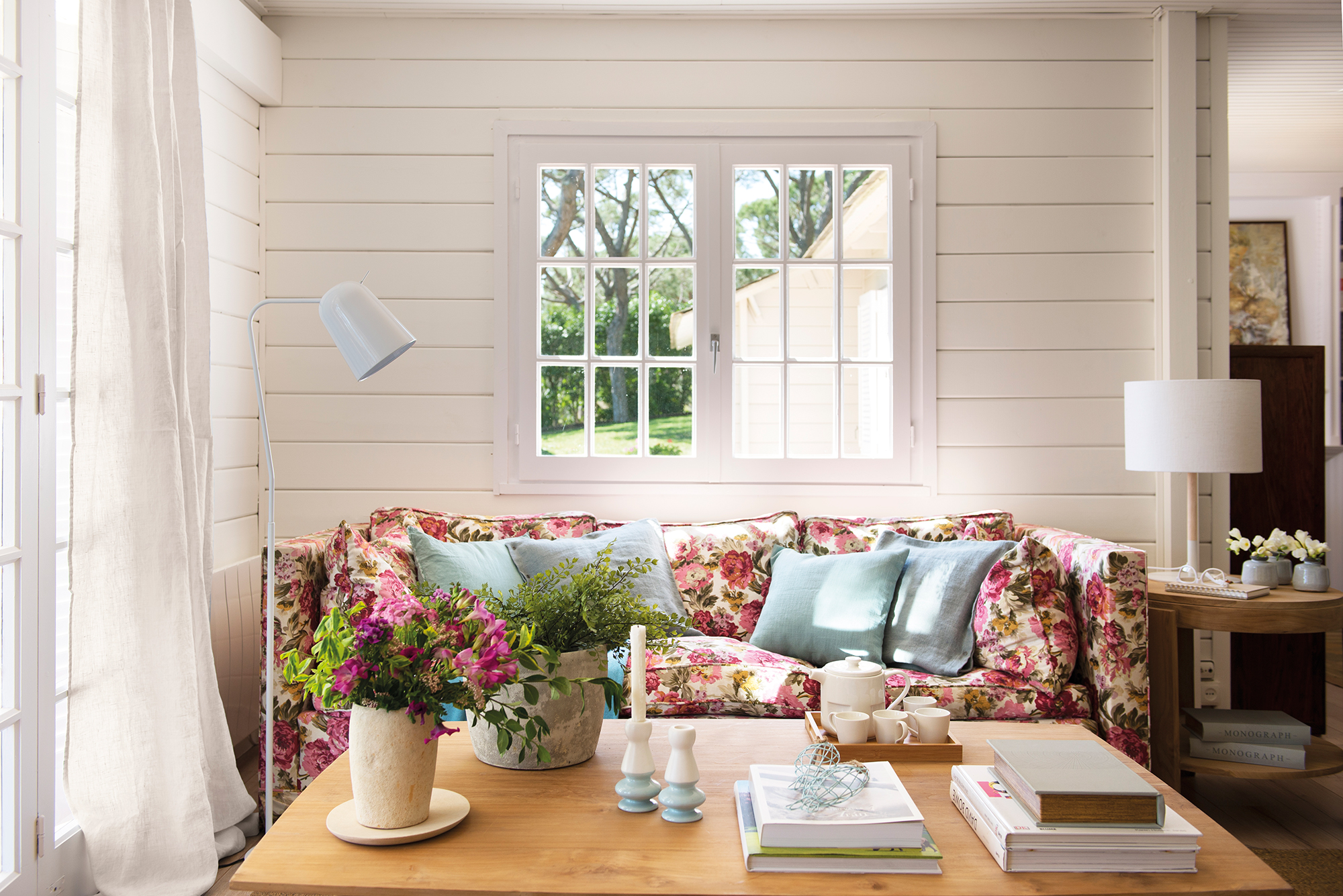 Salón con paredes revestidas de madera en blanco y sofá tapizado de flores