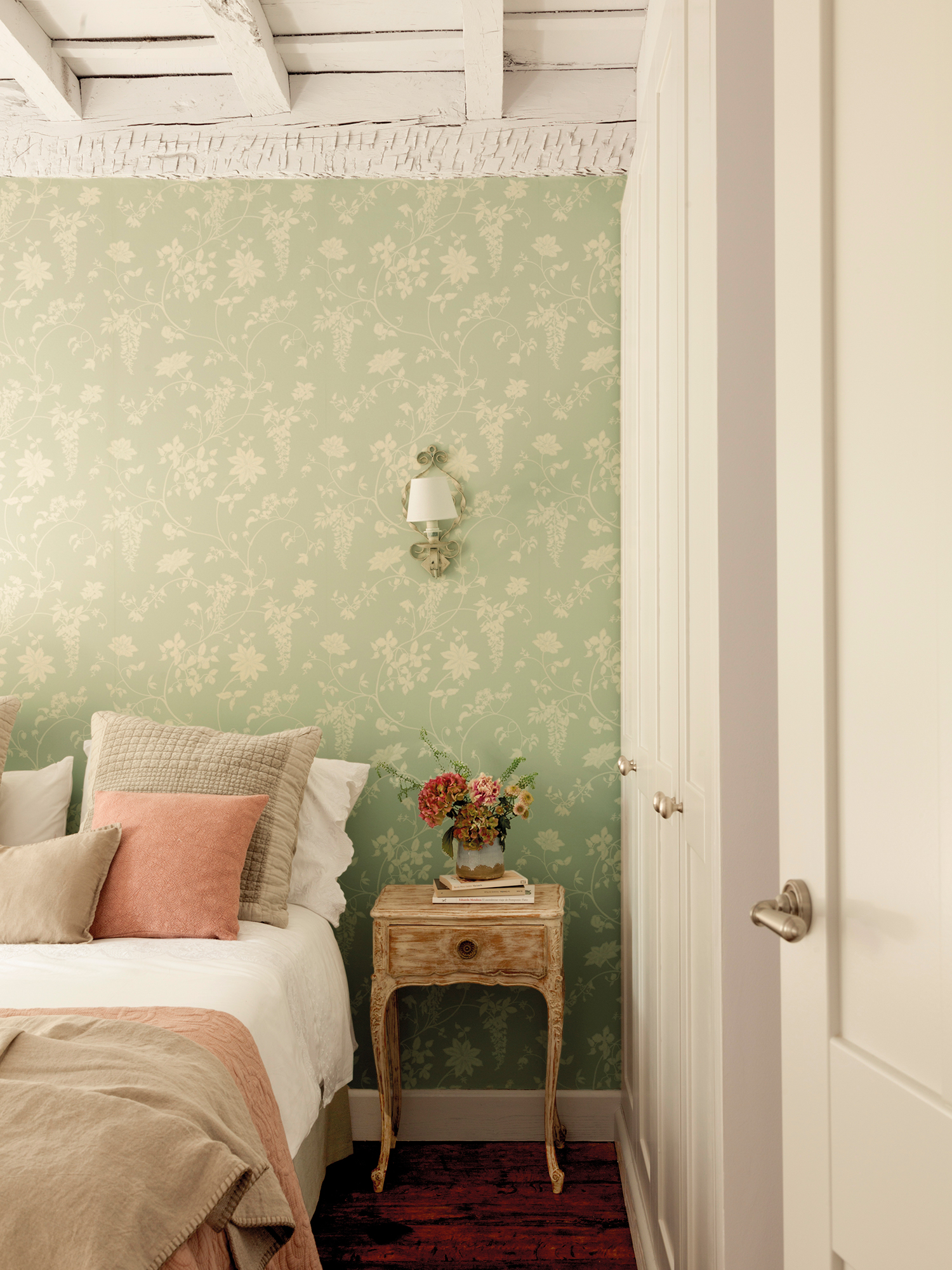 Dormitorio con papel pintado floral vintage y mesita de noche antigua
