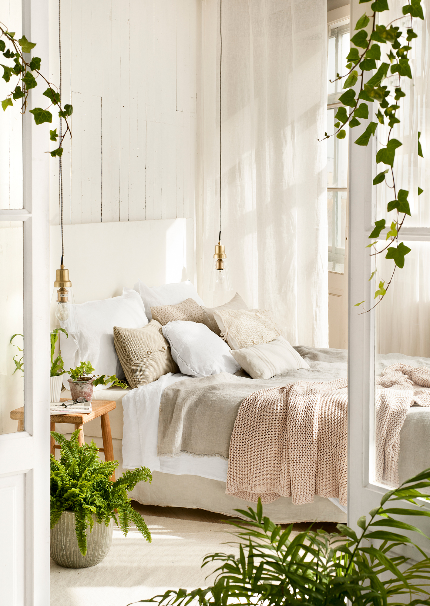 Dormitorio con plantas y ropa de cama blanca. 