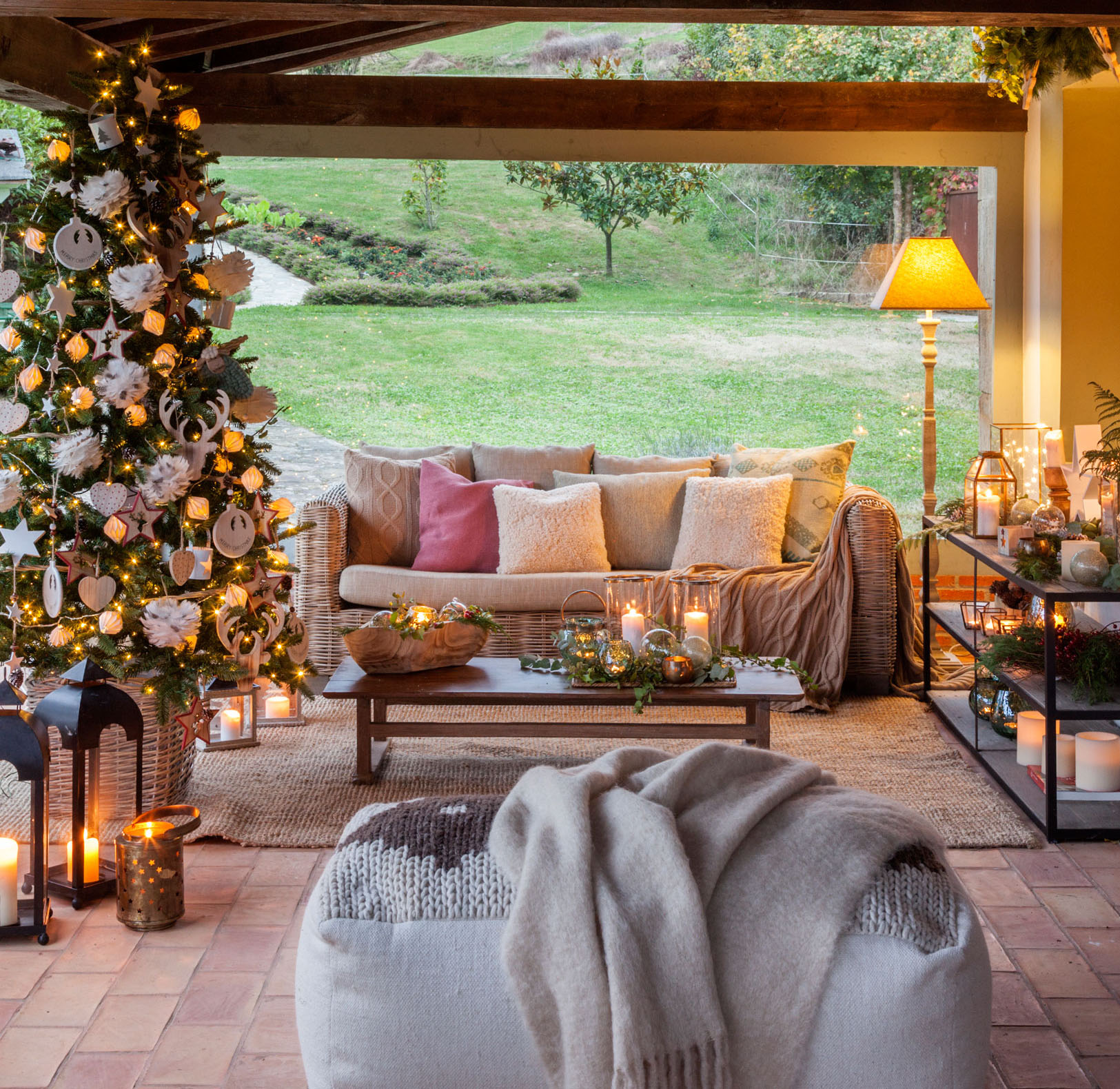 Terraza con sofá de fibra vegetal, puf de punto y árbol de Navidad bien iluminado. 