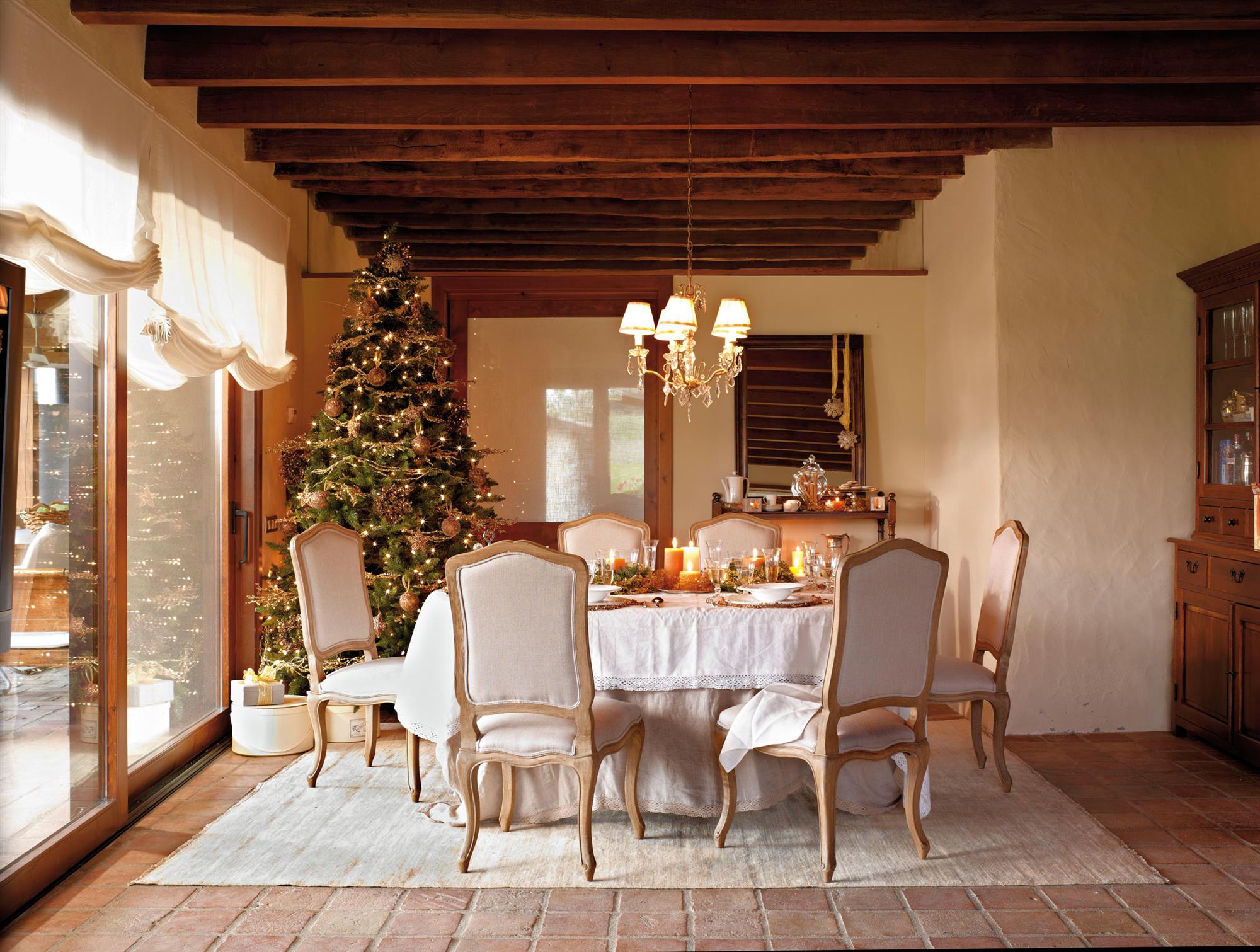 Comedor clásico con mesa navideña, vigas de madera en el techo y árbol de Navidad alto decorado con adornos dorados. 