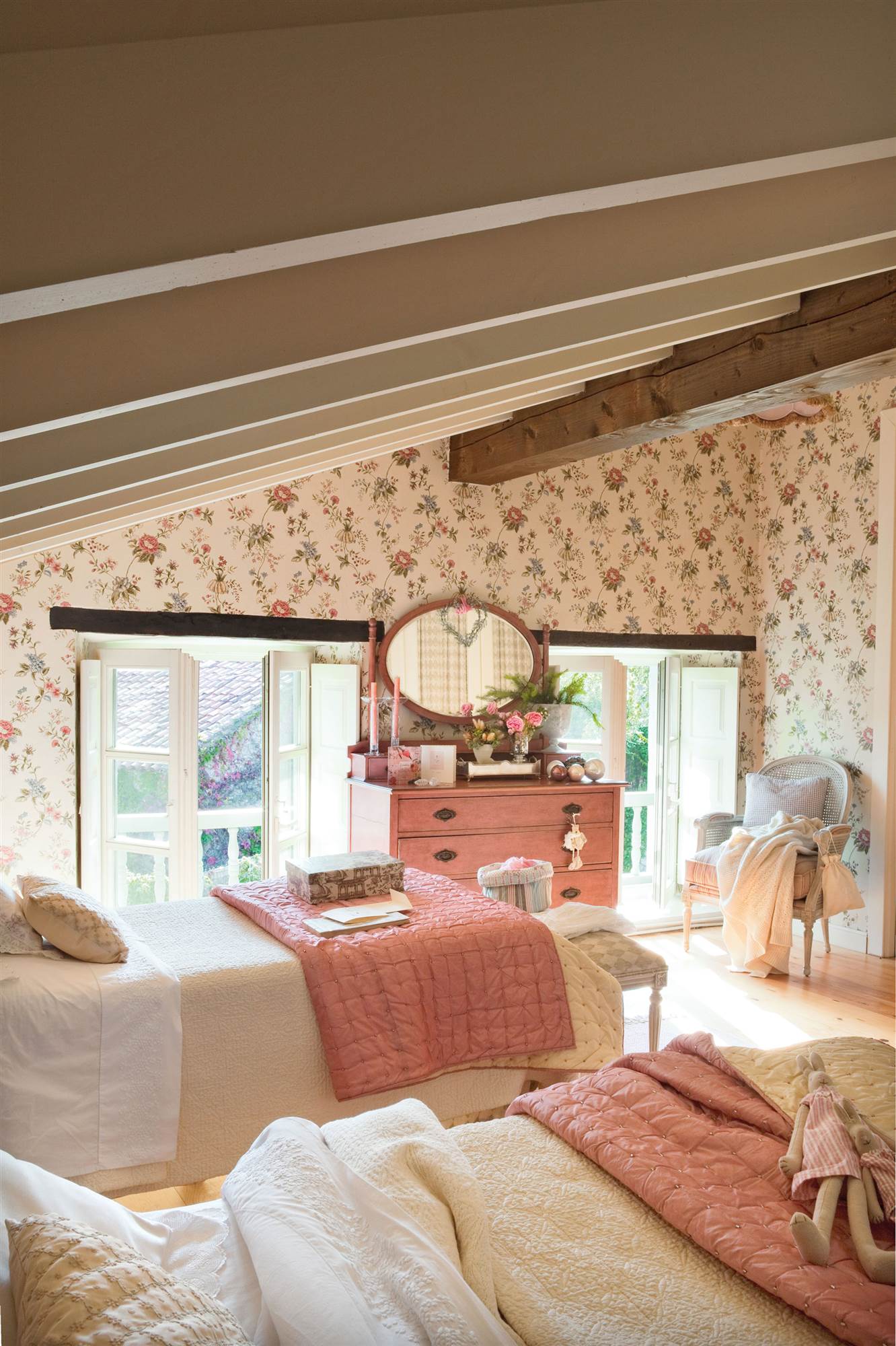 Dormitorio infantil abuhardillado con papel pintado floral y dos camas iguales.