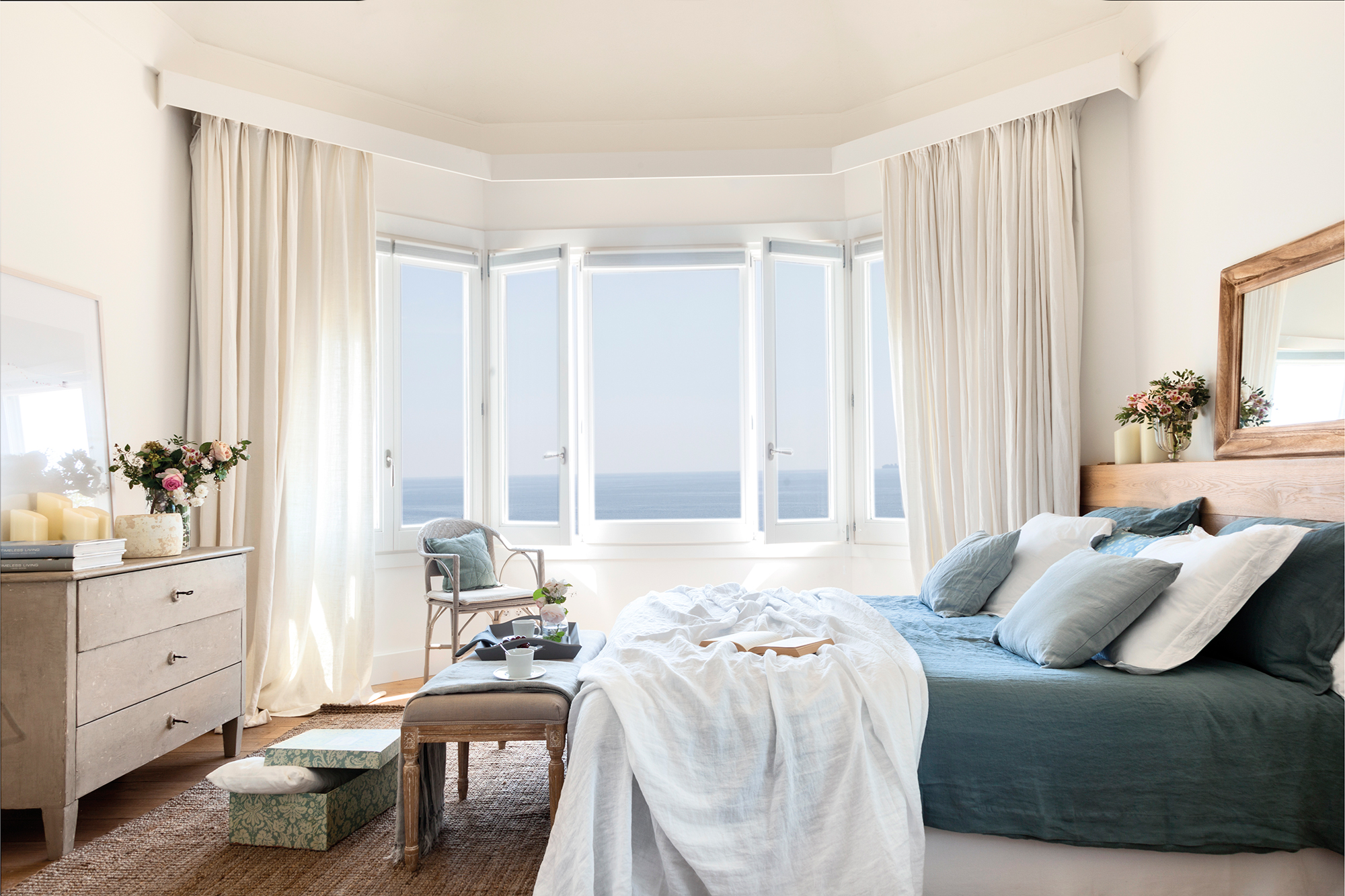 Dormitorio con dormitorio con ropa de cama azul claro, ventanales y cortinas blancas.