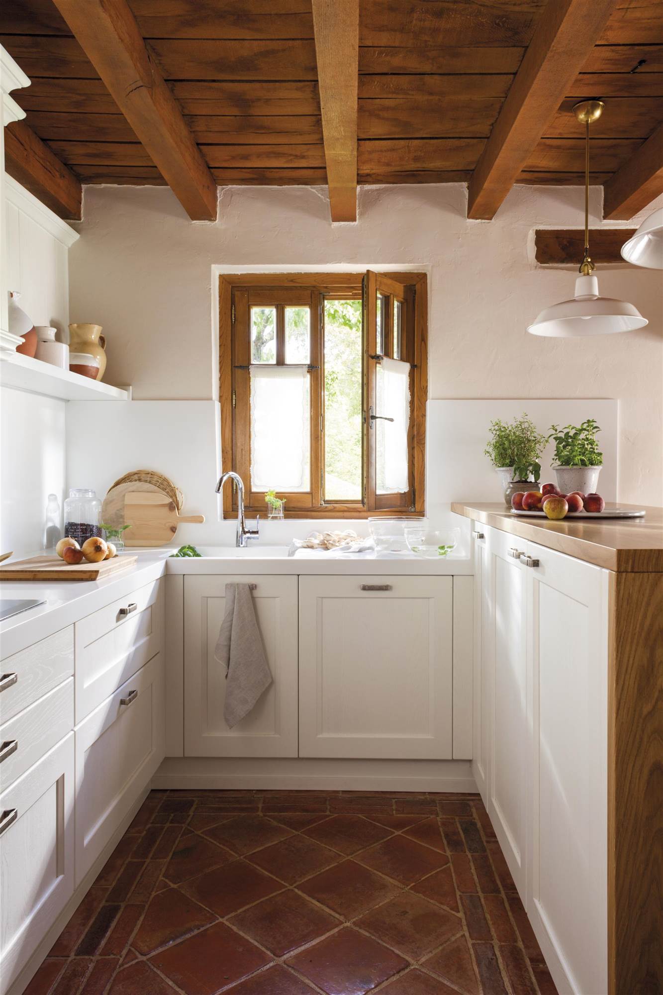 Small white kitchen are mud floors and a wooden ceiling with beams. 