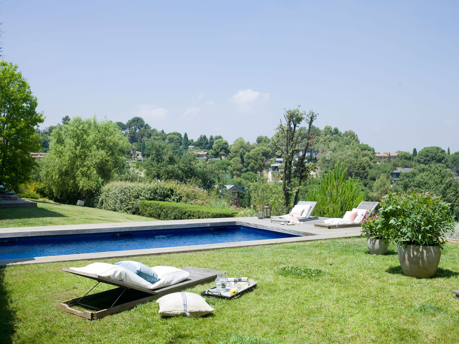 Jardín con piscina con pavimento de madera. Tumbonas de diseño de Cristina Franch.