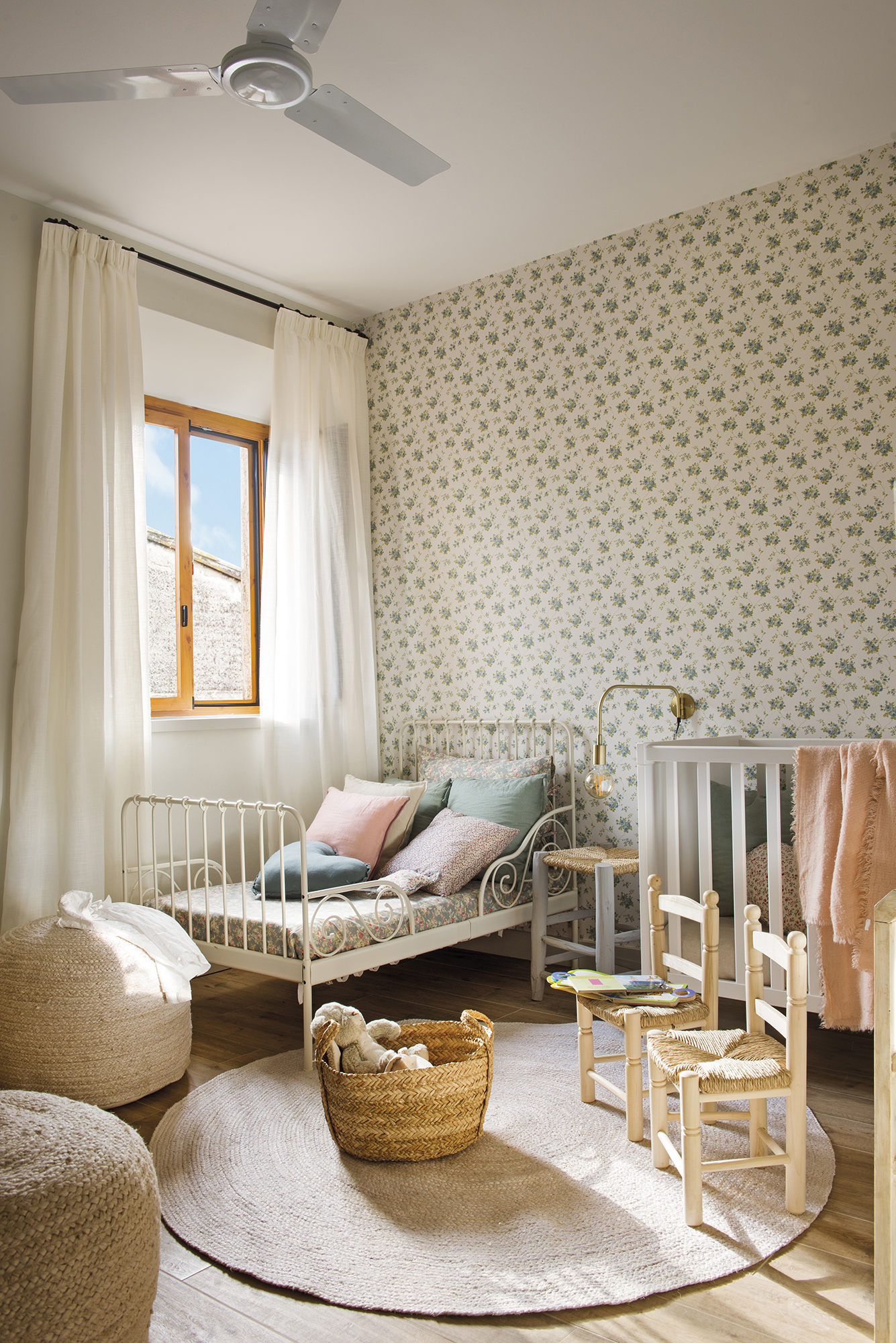 Dormitorio infantil con papel pintado de motivos florales pequeños y camas de forja blanca. 