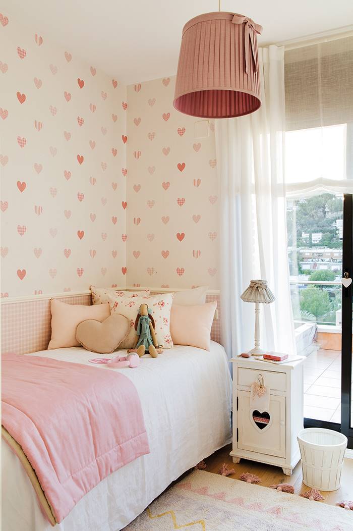 Habitación infantil en blanco y rosa con pared con papel pintado de corazones.