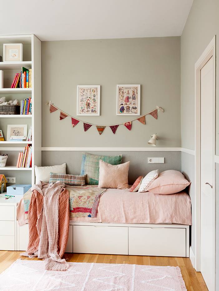 Habitación infantil con camita rosa, guirnalda y estantería. 