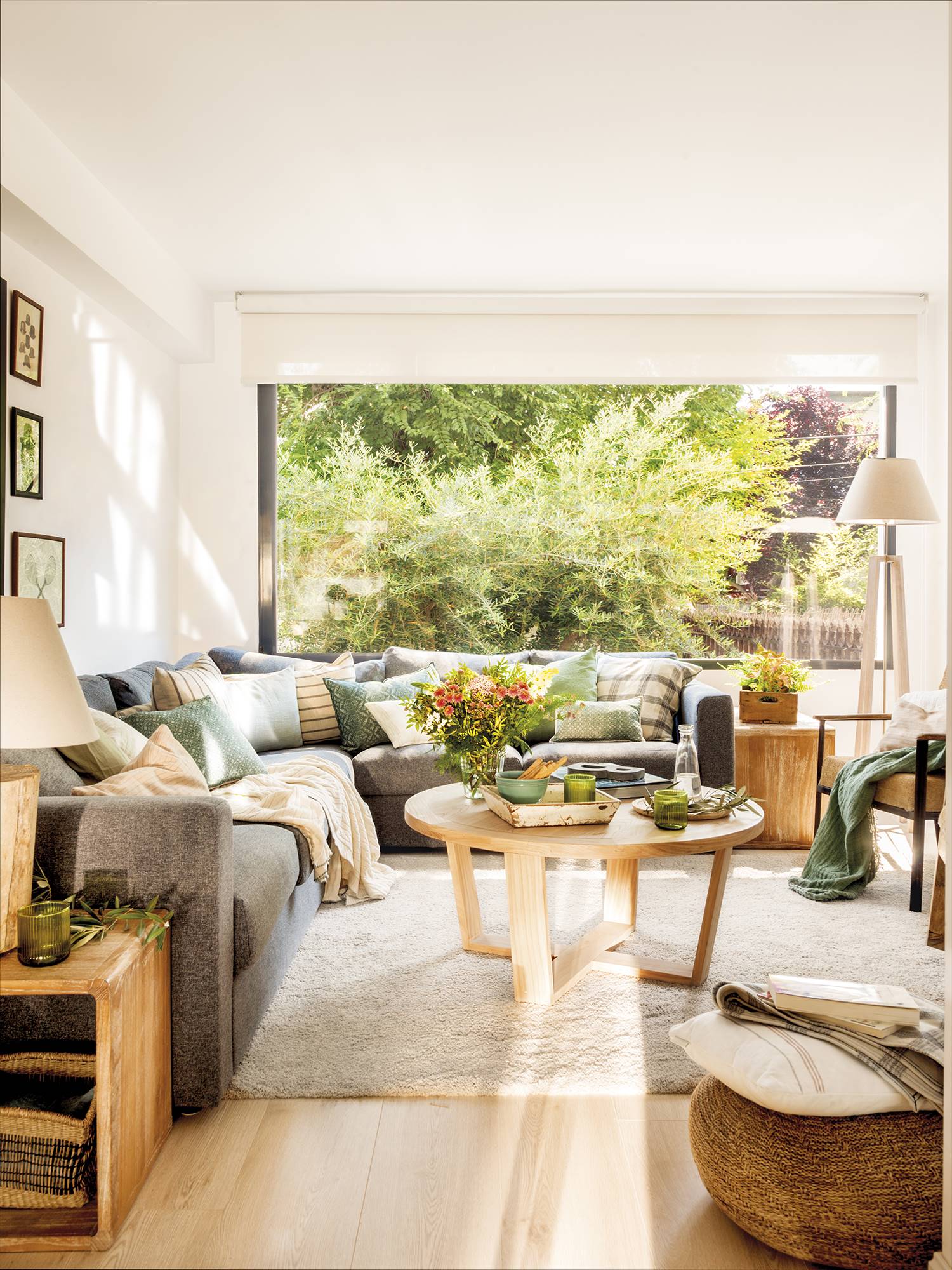 Salón con sofá gris, alfombra de pelo, mesa de centro de madera redonda y gran ventanal.