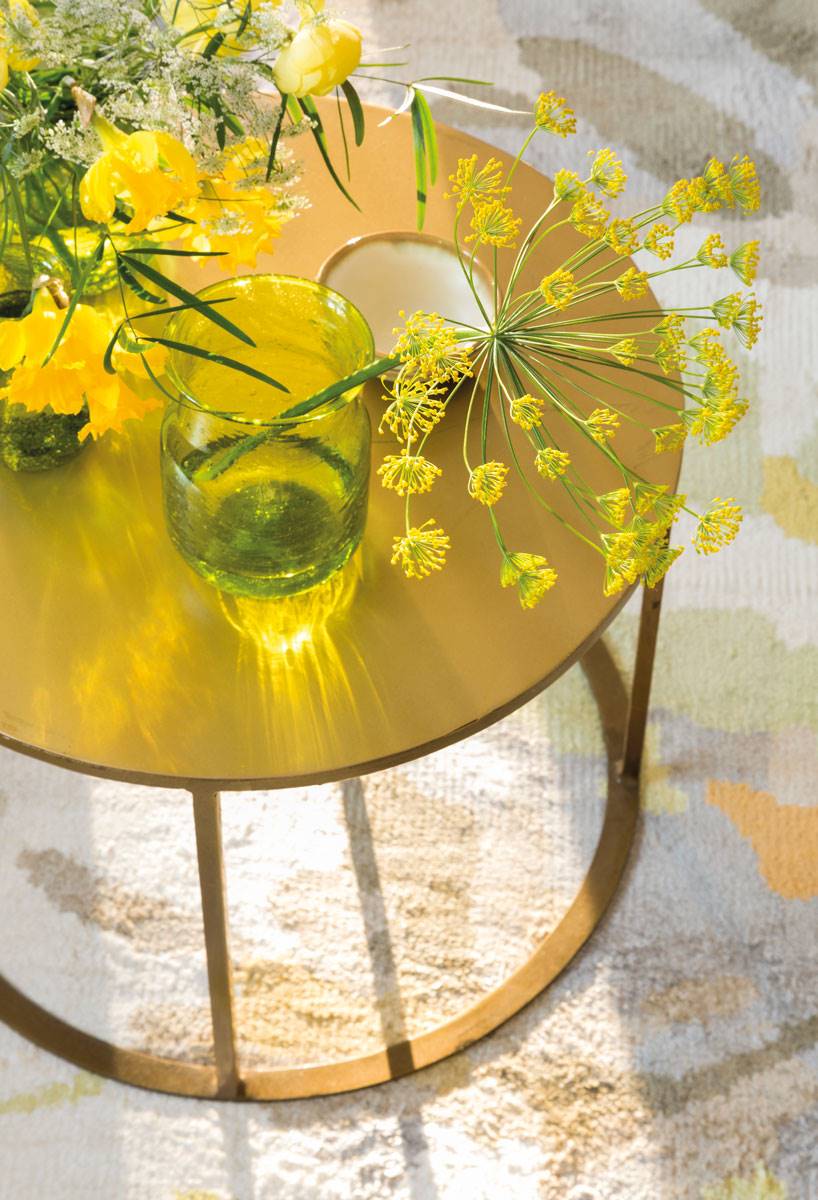 Mesa auxiliar redonda y dorada con jarrón con flores.