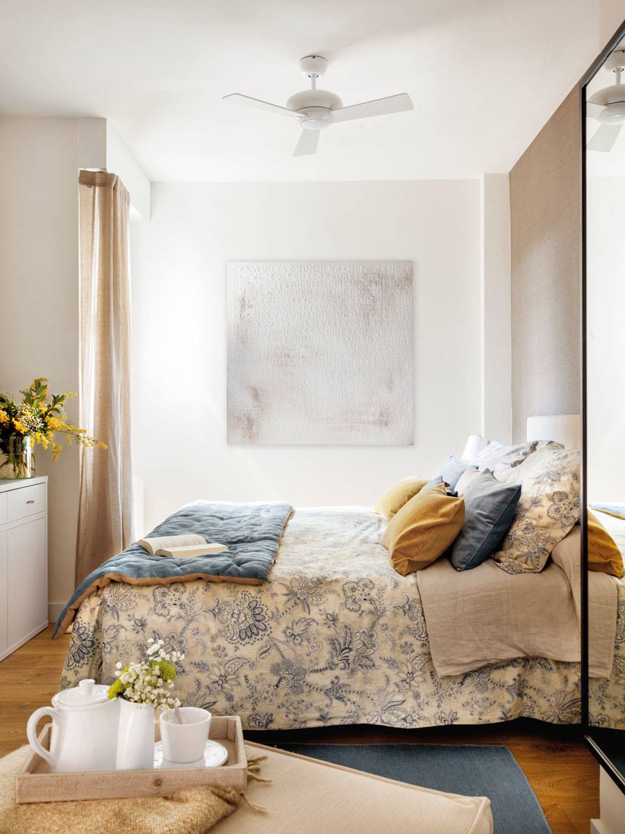 Dormitorio con colcha de flores y ventilador.