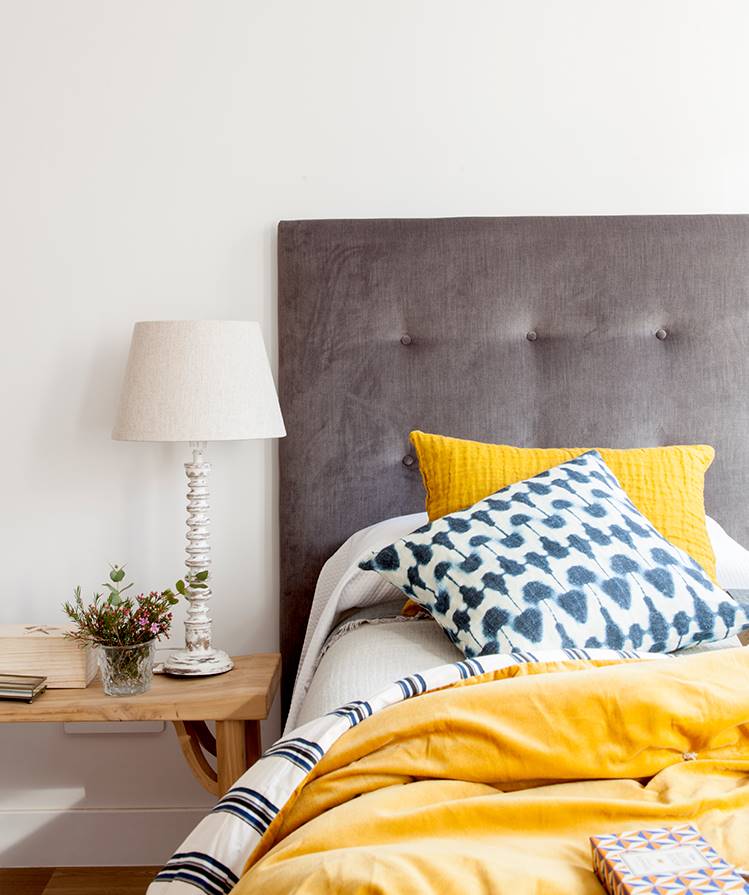 Dormitorio con ropa de cama amarilla y cabecero tapizado gris.