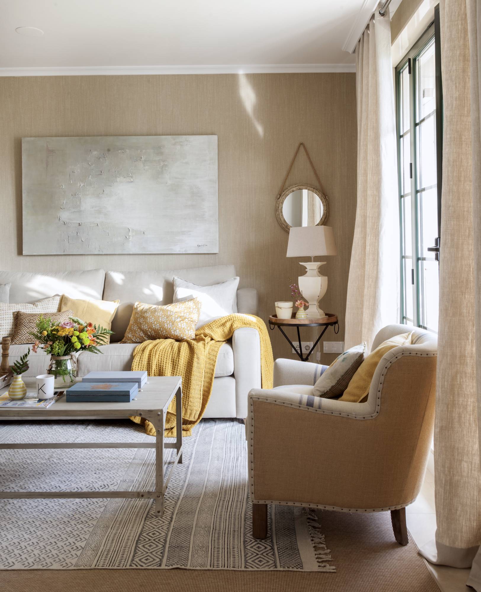 Salón con paredes beige y sofá blanco, con cojines de color mostaza. 