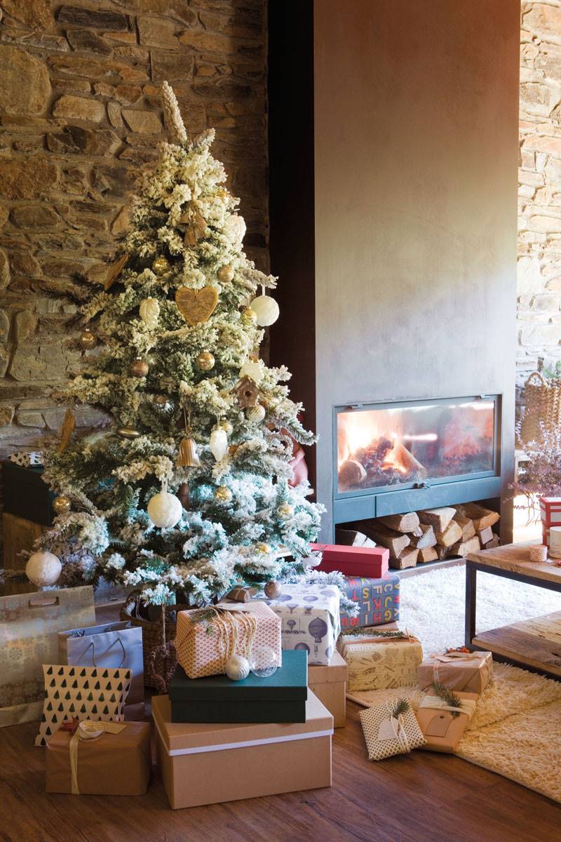 Salón rústico con chimenea y árbol de Navidad nevado con aires de montaña.
