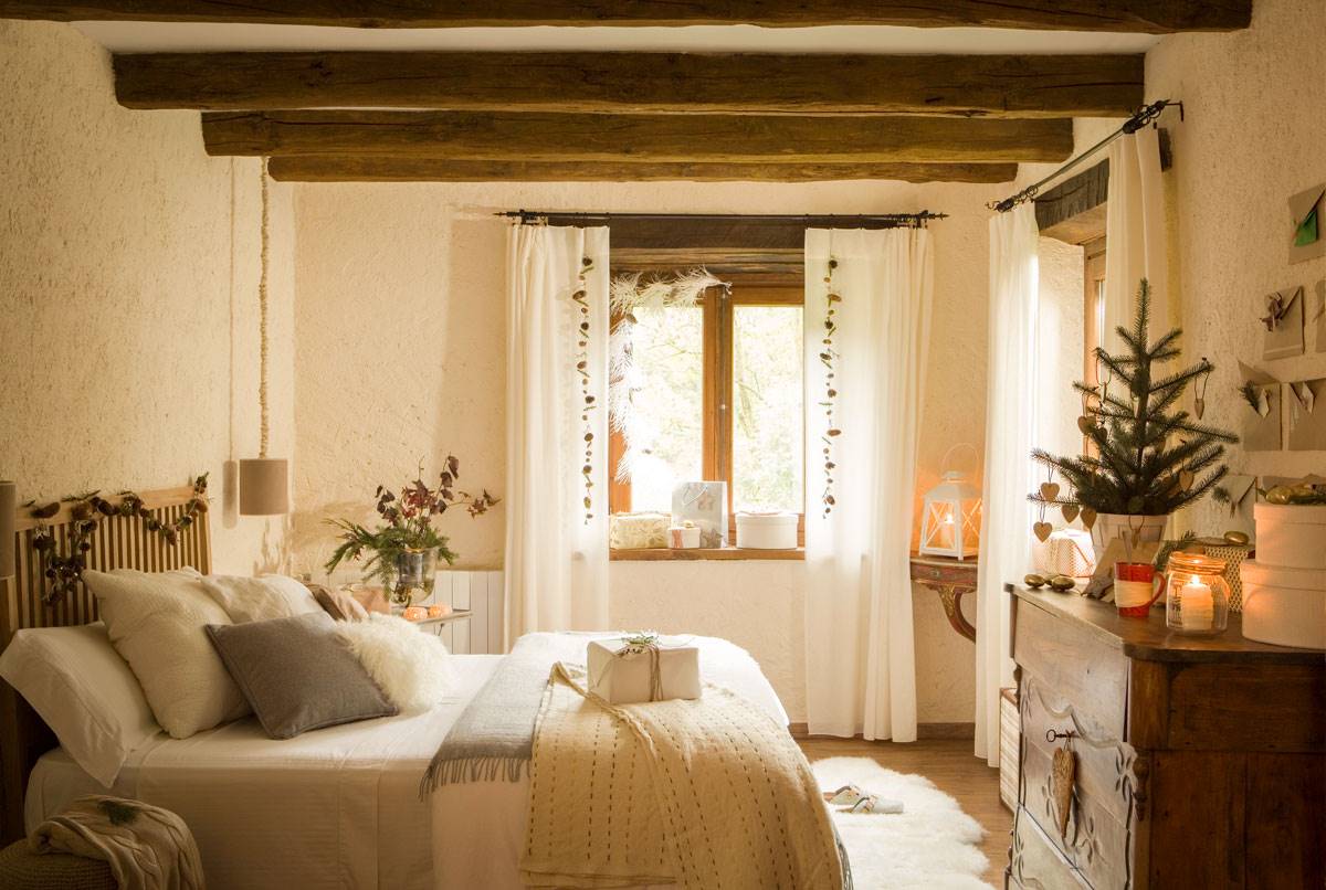 Dormitorio rústico con vigas, cómoda de madera y árbol de Navidad encima tamaño mini. 