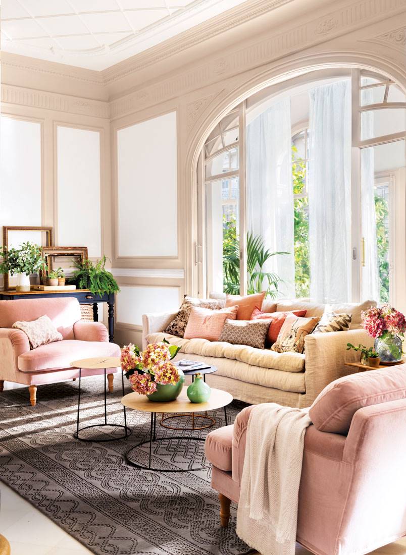 Salón regio con gran ventanal y distribución en "U" de sofá y butacas rosas.