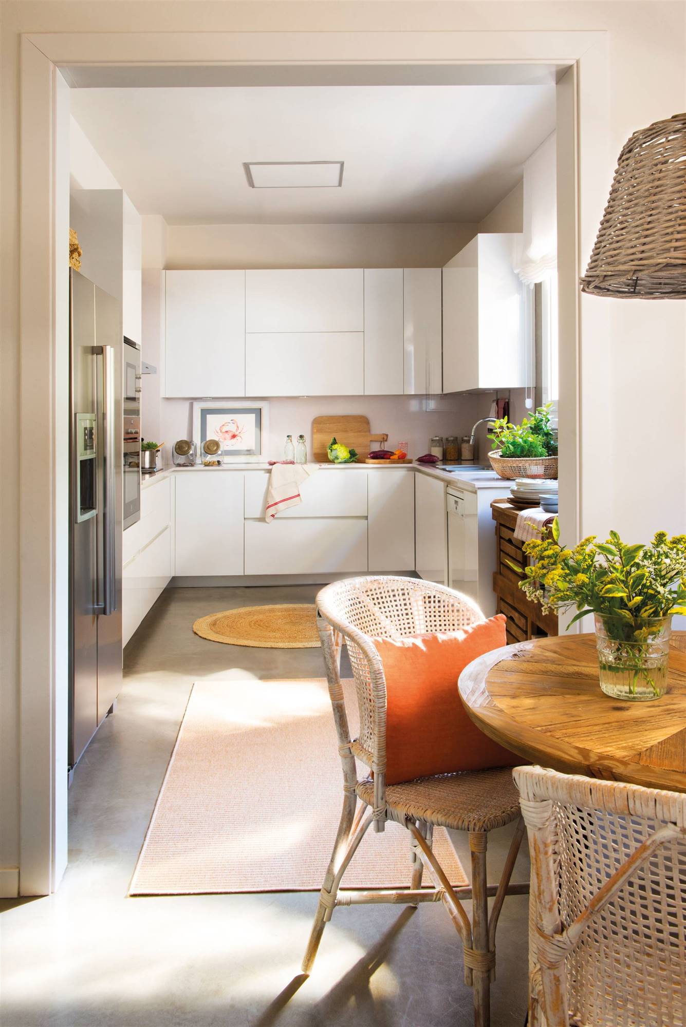 Moderna cocina abierta al comedor con muebles blancos sin tiradores, detalles de fibras y electrodomésticos de acero inoxidable.