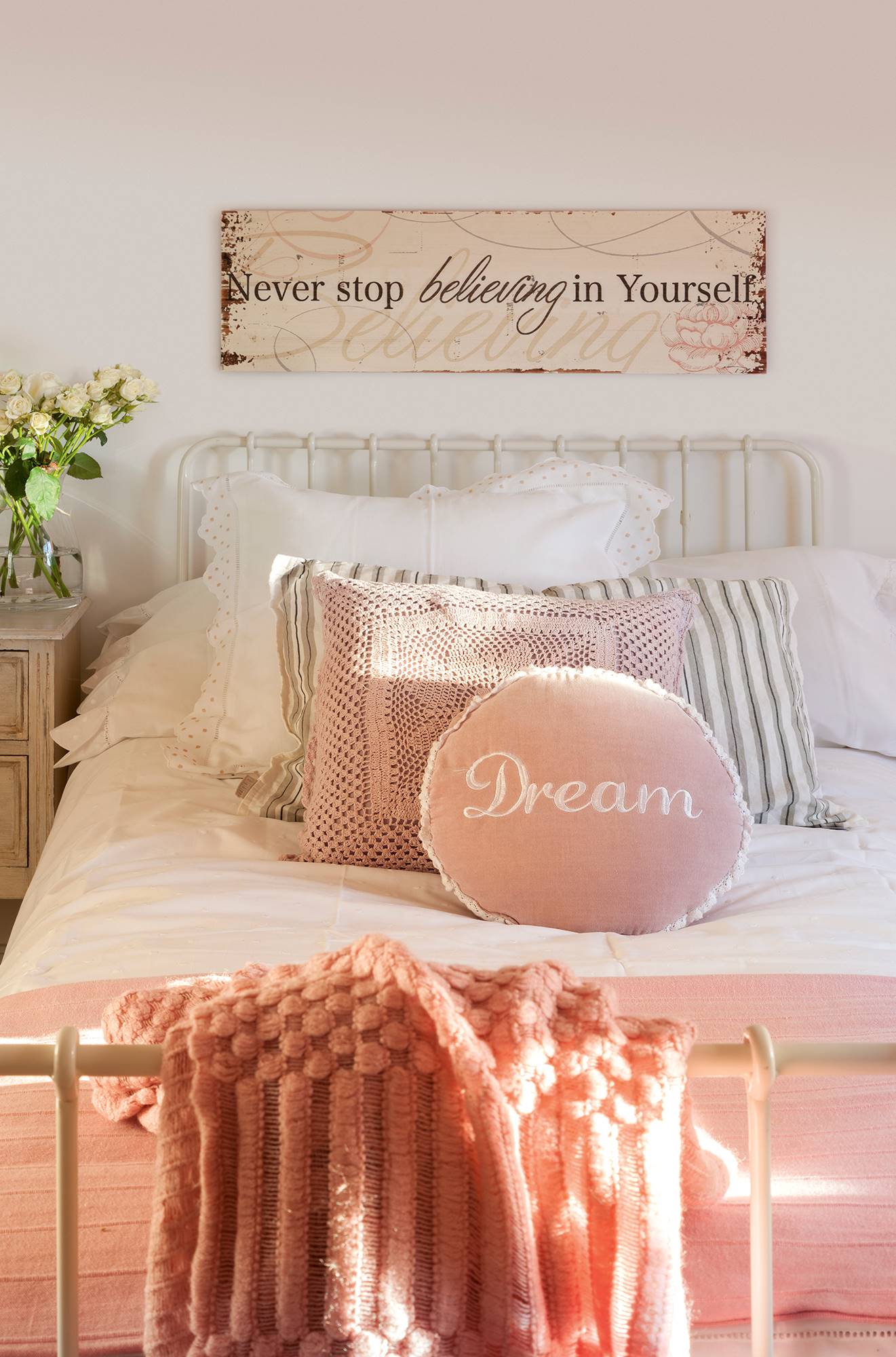 Dormitorio con cabecero metálico y ropa de cama blanca y rosa. 