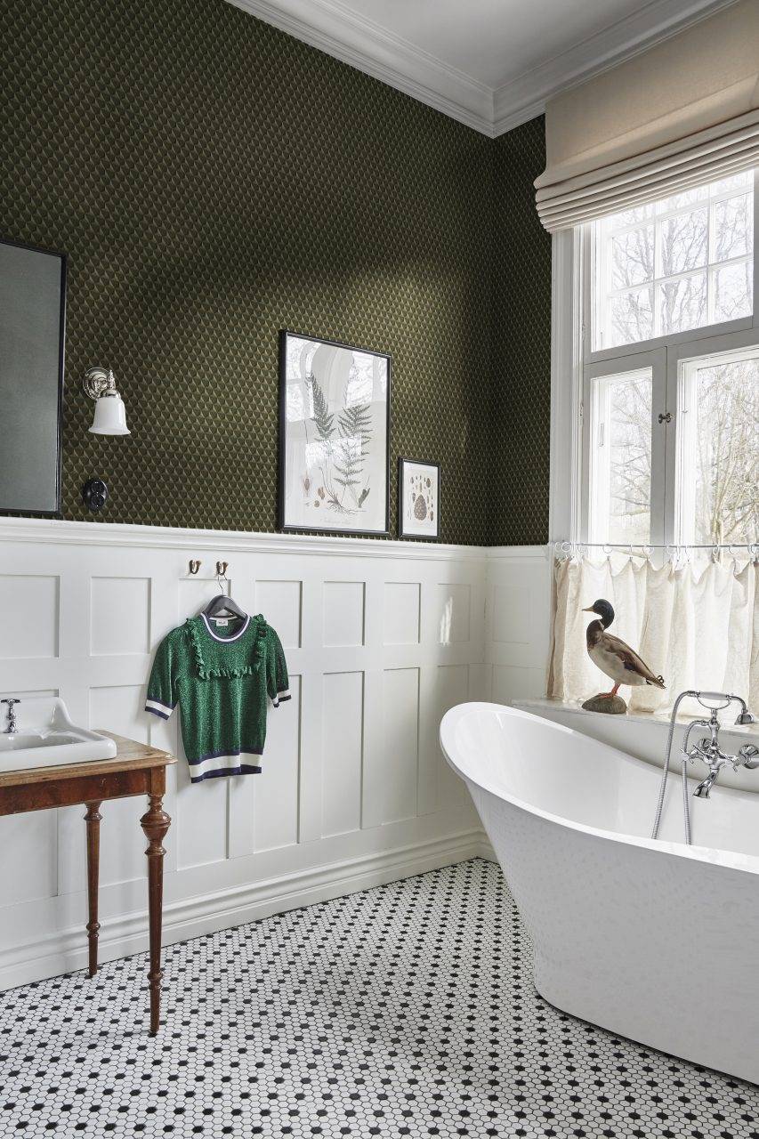 Baño con arrimadero blanco de cuarterones y papel pintado de dibujos geométricos en verde.