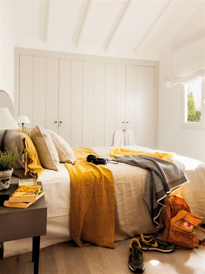 Dormitorio con paredes en blanco y ropa de cama beige y mostaza