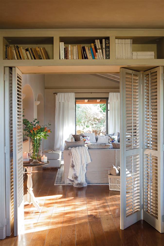 Puerta de acceso al salón cerrada con persianas de madera y con espacio para guardar libros