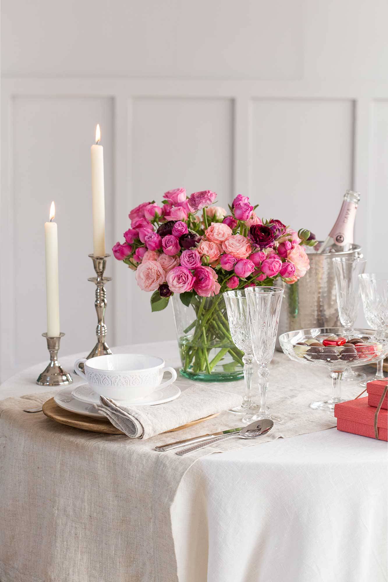Mesa vestida y con un jarrón con rosas rosas. 