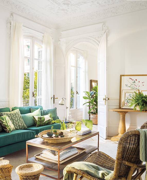 Salón señorial blanco con sofás verdes y molduras en techos y paredes. 
