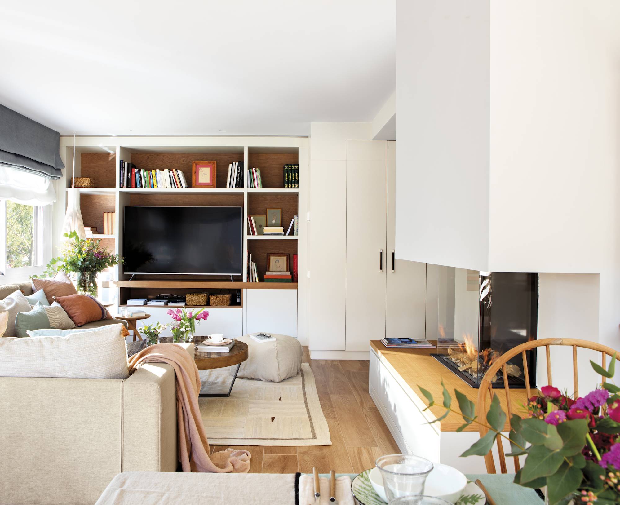 Salón con sofá beige, librería que integra el televisor y chimenea moderna. 