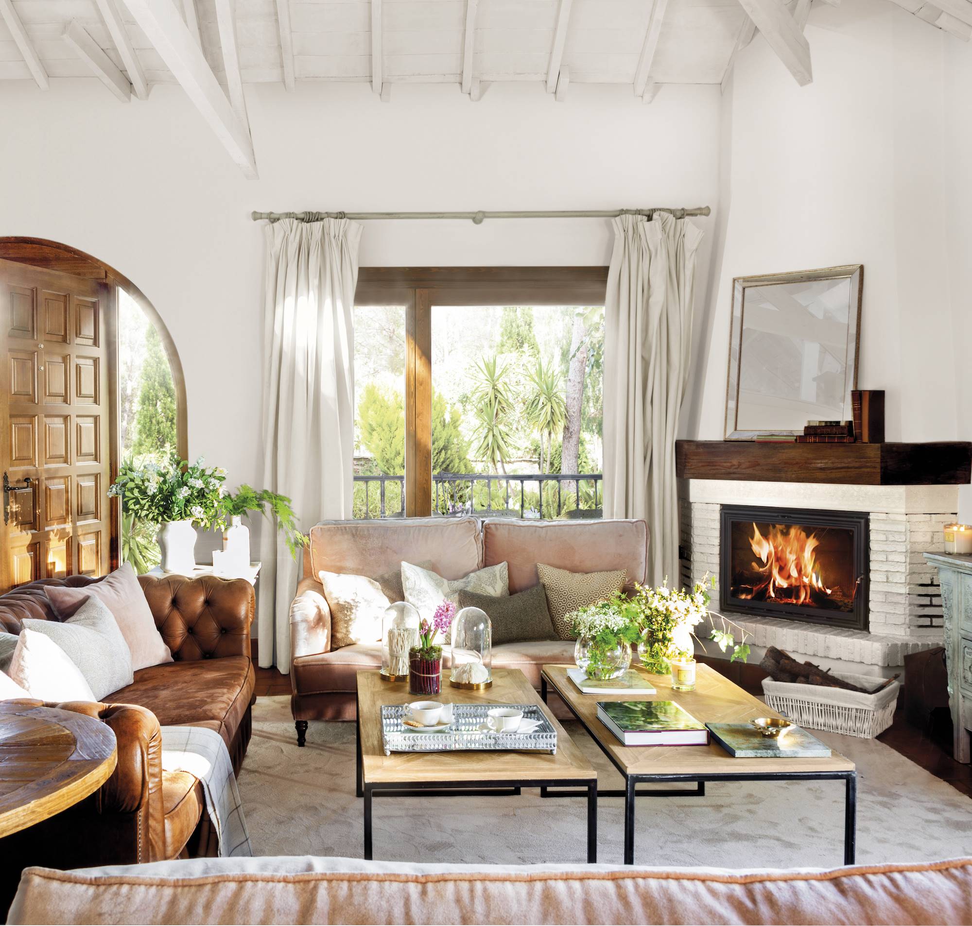 Salón rústico con chimenea en esquina, sofá chéster de cuero y mesas de centro de madera.