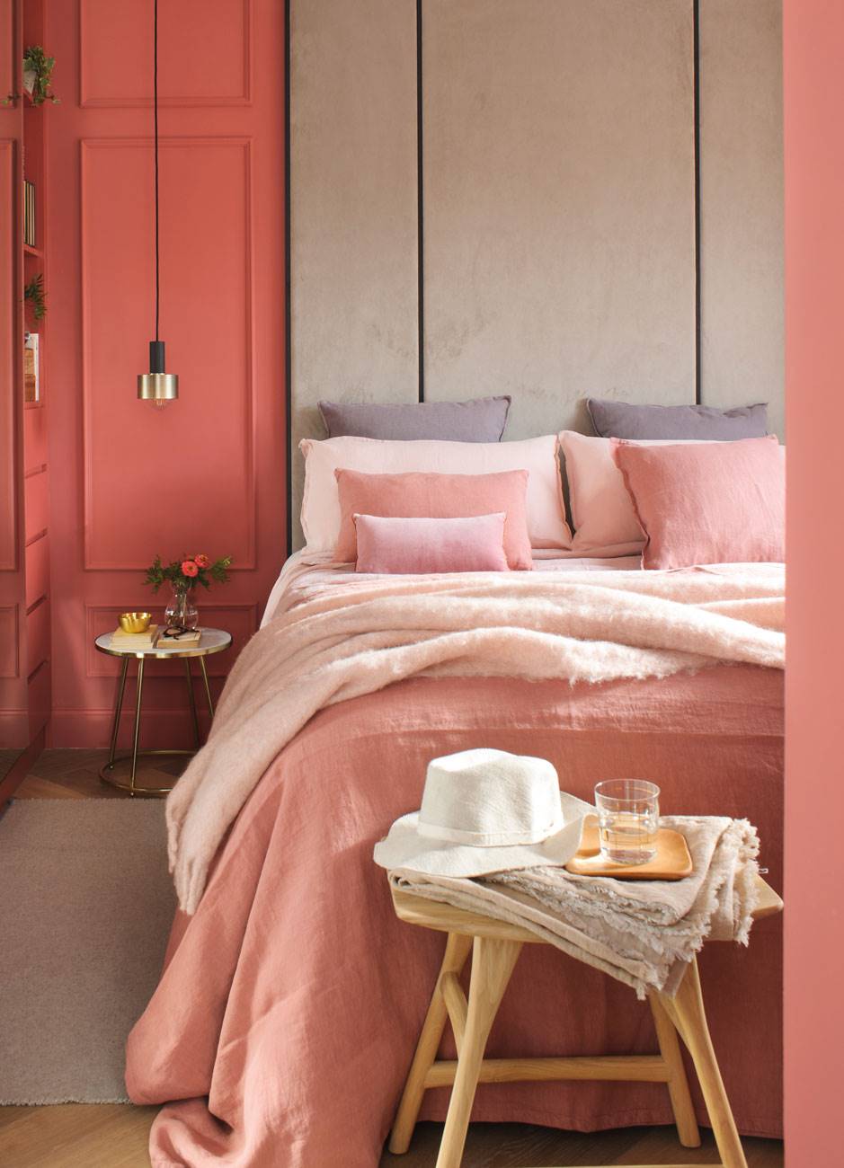 Dormitorio con paredes color rosa y cabecero tapizado hasta el techo. 