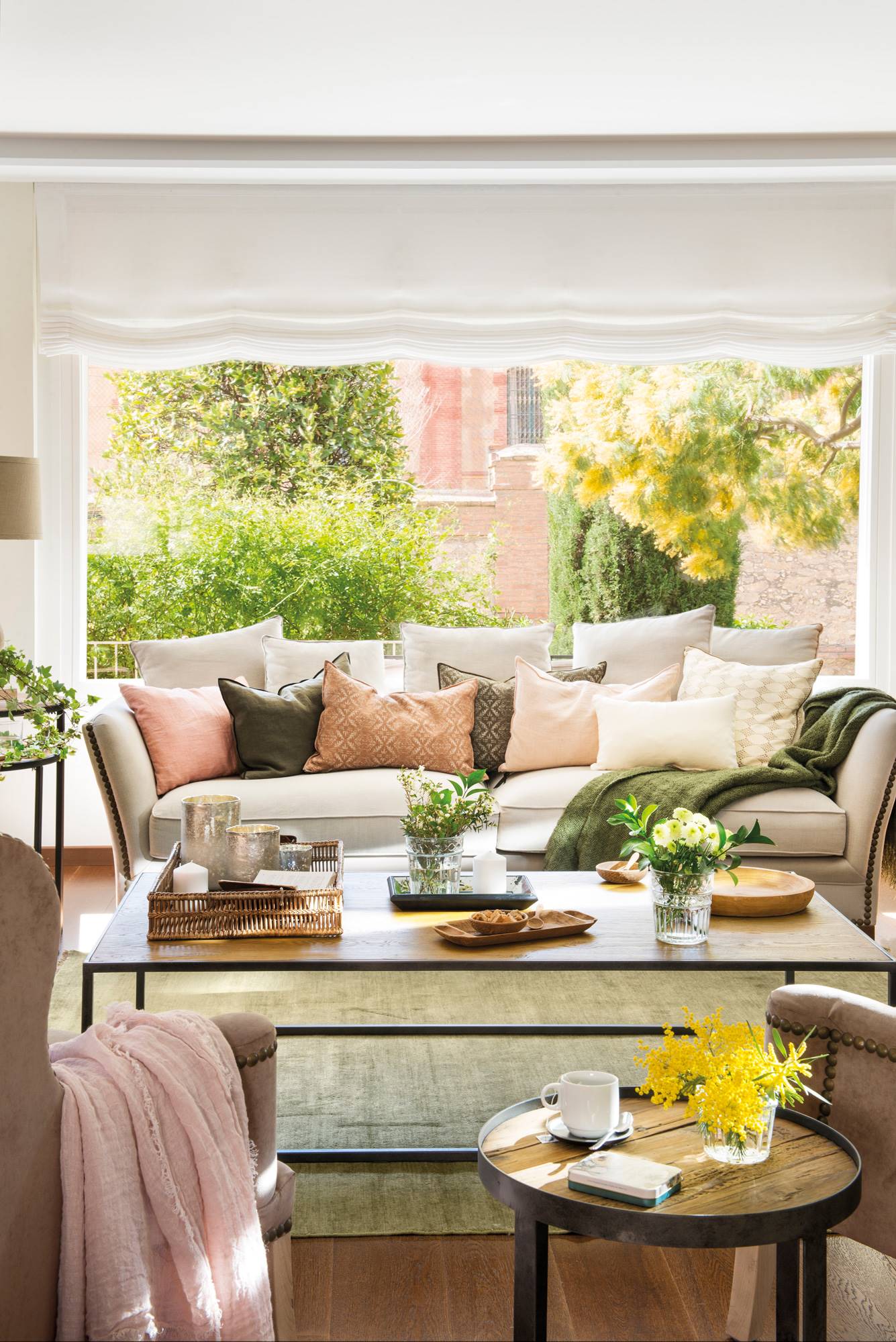 Salón de primavera con sofá blanco delante de la ventana y cojines en tonos pastel.