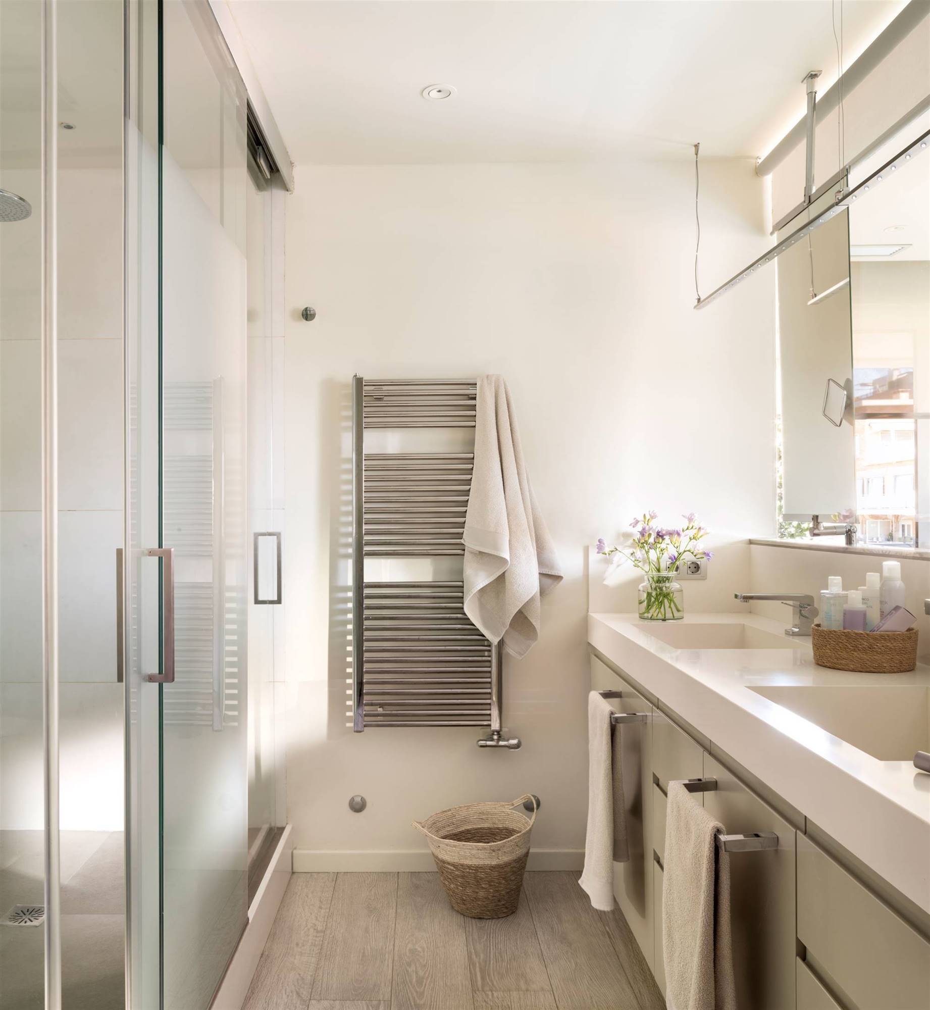 Baño alargado con lavamanos a un lado y cabinas con ducha e inodoro. 