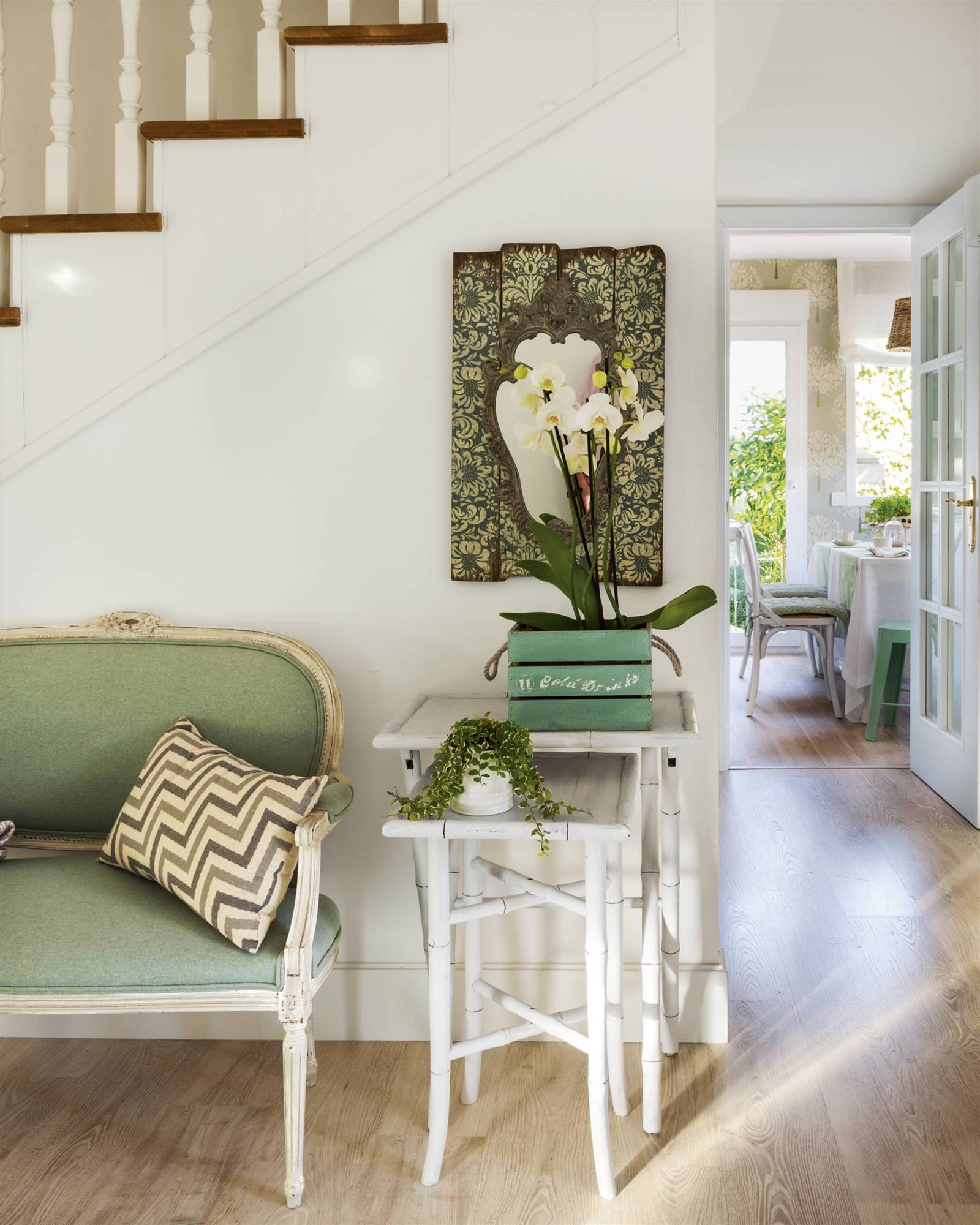 Recibidor con banco tapizado en verde y mesas nido blancas.