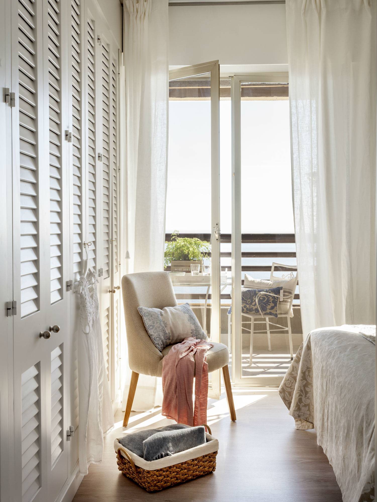 Dormitorio veraniego con armarios blancos y un sillón en color beige. 