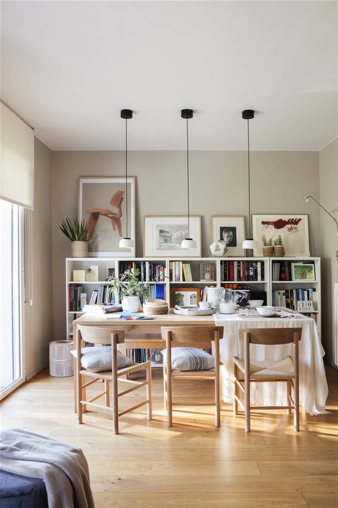 Mesa de comedor de madera con lamparas colgantes y librería blanca de pared a media altura 00493650_O