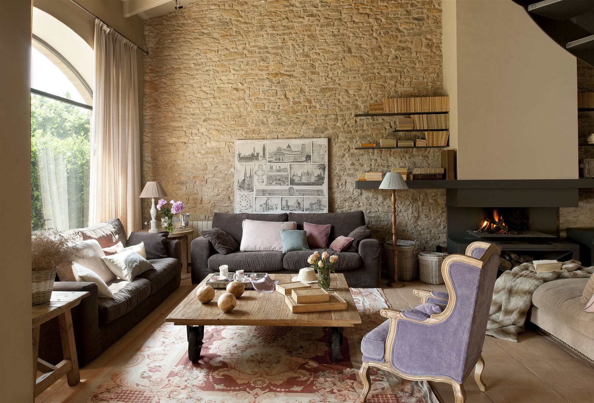 Salón rústico con pared de piedra y sofás clásidos de color gris. 